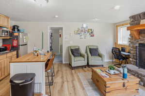 Open concept living space featuring wood-finish flooring, a stone-clad fireplace with a substantial wood mantel, and an integrated kitchen island with a wood countertop