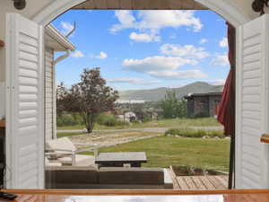 Arched doorway featuring bi-fold louvered shutters, opening to an exterior patio with wood decking and a landscaped yard