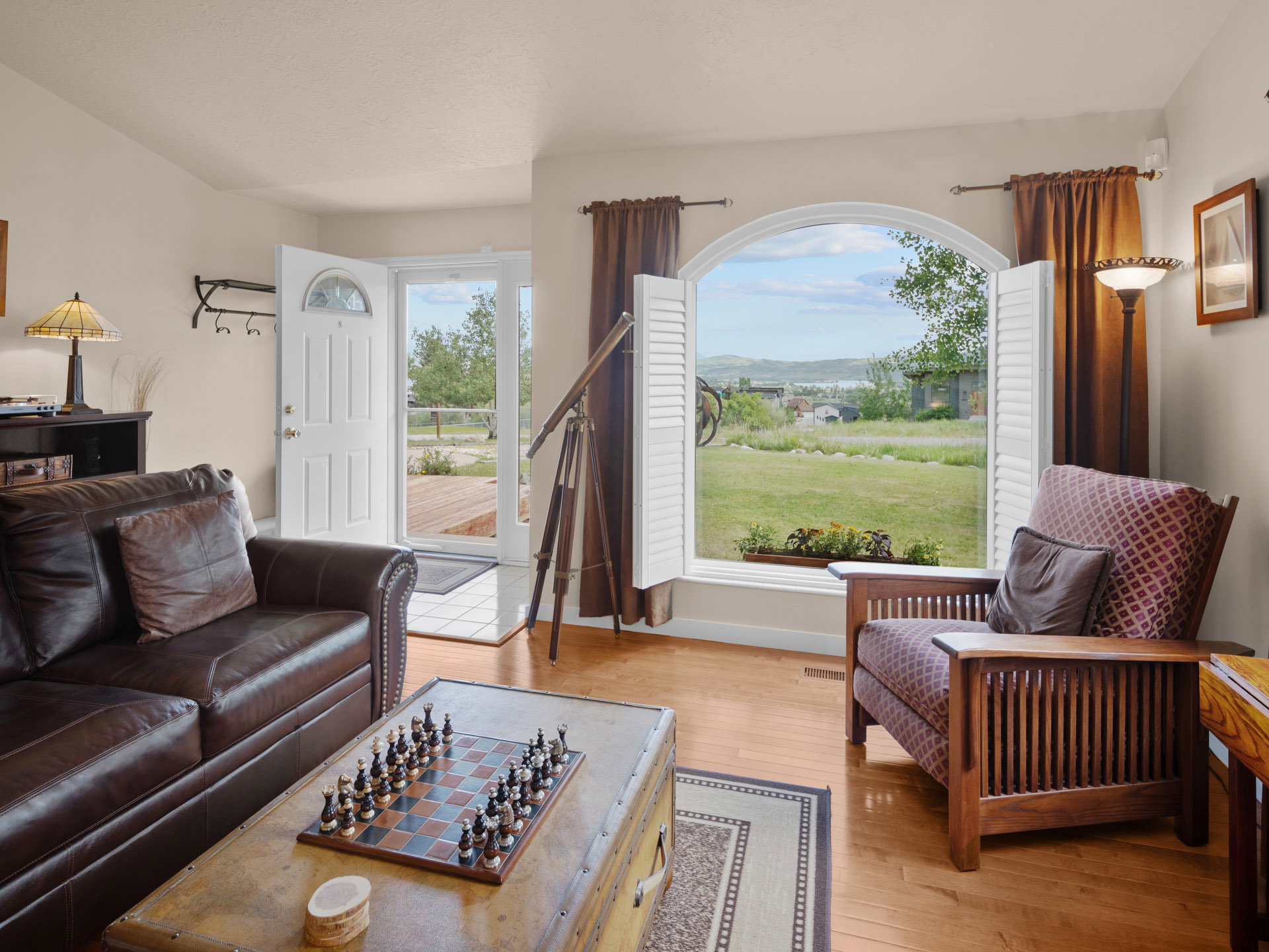 Living area featuring wood-finish flooring, a large arched window with interior shutters, and a white paneled entry door