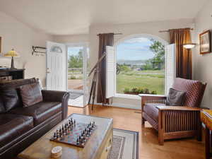 Living area featuring wood-finish flooring, a large arched window with interior shutters, and a white paneled entry door