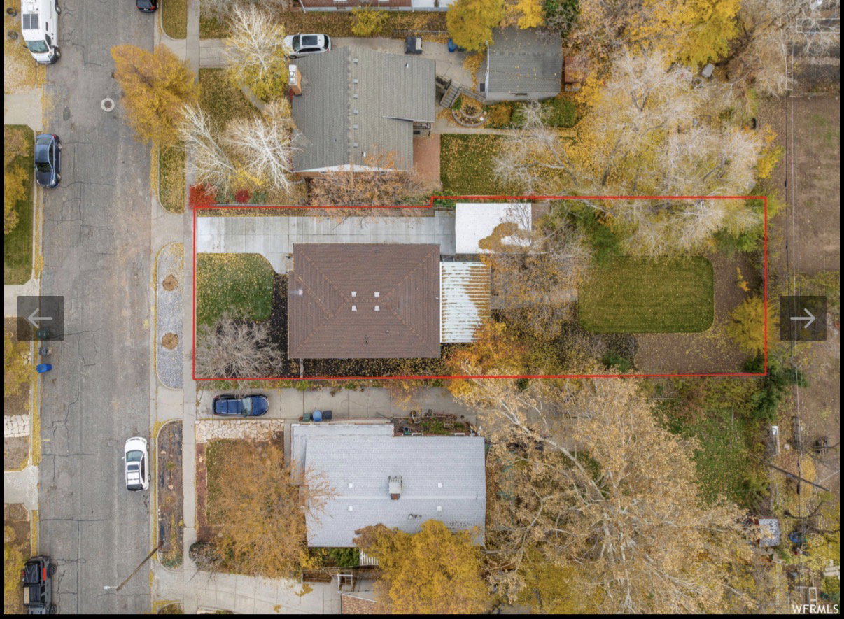 Aerial perspective of a property featuring a single-story residence with a brown shingled roof, a paved driveway, and a front lawn