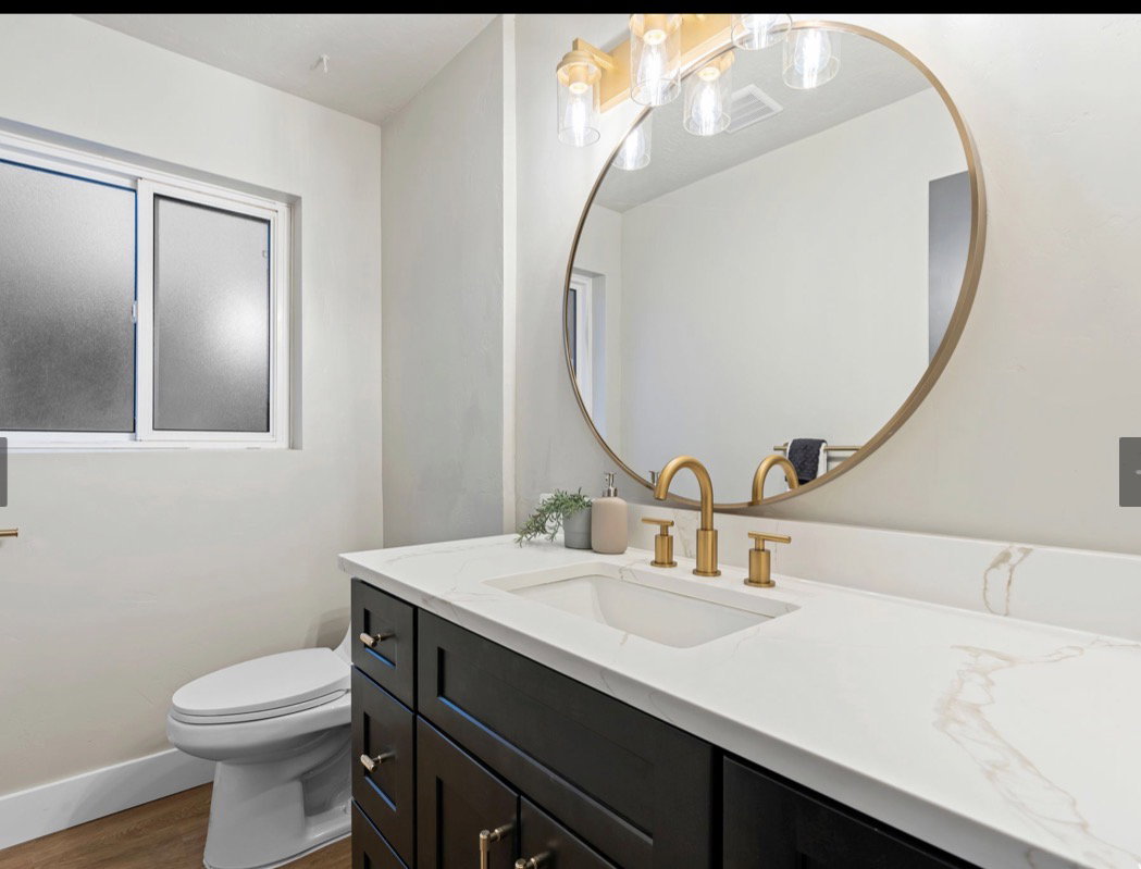 Modern bathroom featuring a dark wood vanity with gold hardware, a white countertop with subtle veining, and a gold-framed circular mirror
