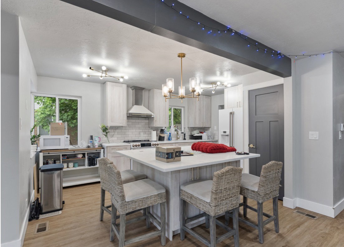 Kitchen featuring a center island with seating, white shaker cabinetry, stainless steel appliances, a tile backsplash, and wood-finish flooring