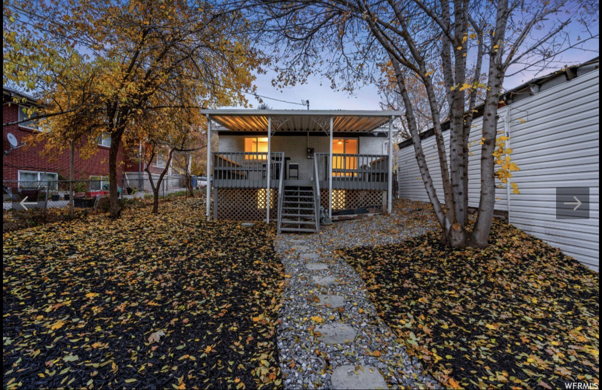 Rear exterior featuring a covered deck with lattice skirting, leading to a flagstone pathway