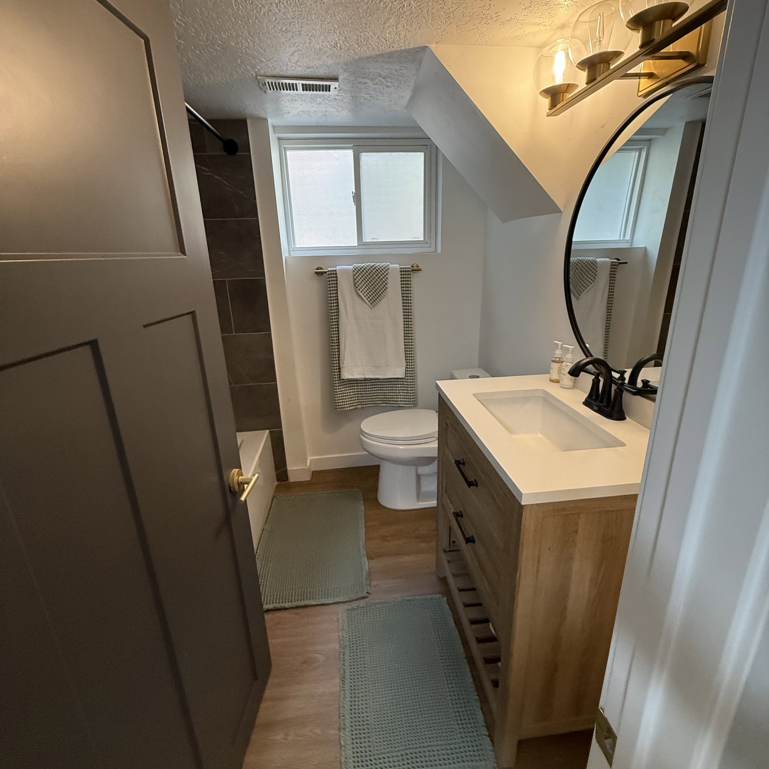 Bathroom featuring a single vanity with a white countertop and wood-finish cabinetry, a circular mirror, and a wall-mounted light fixture