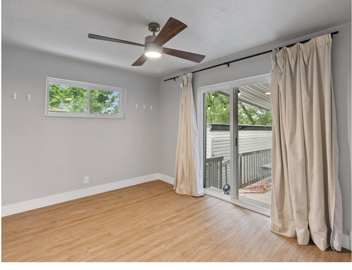 Room featuring wood-finish flooring, a ceiling fan with integrated lighting, and a sliding glass door leading to an outdoor deck