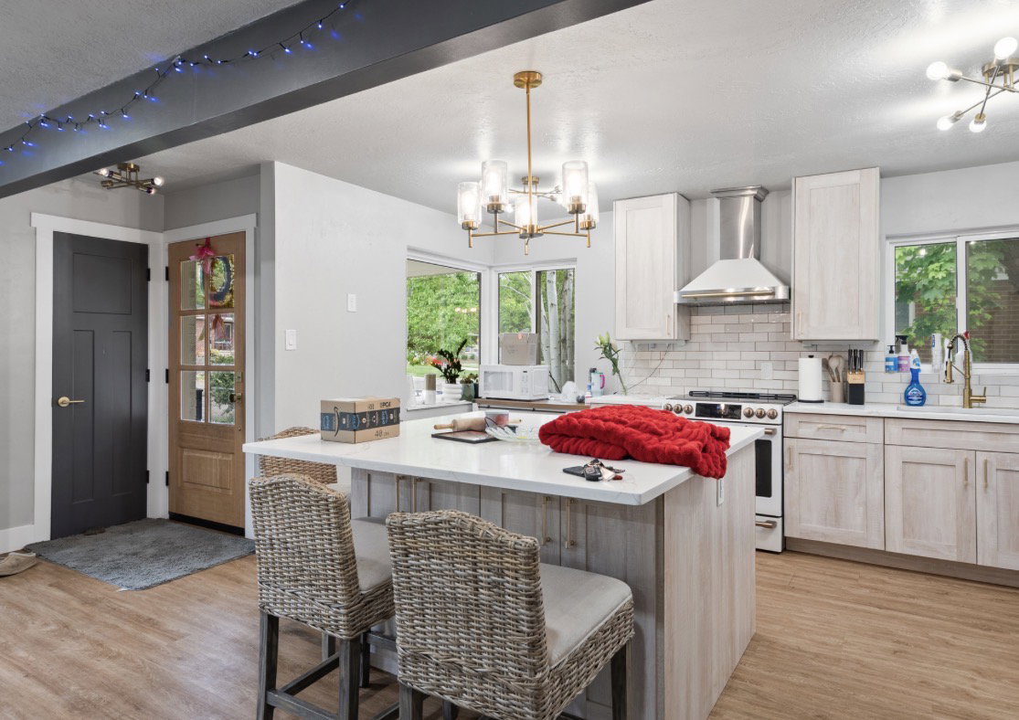 Kitchen featuring a central island with countertop seating, wood-finish flooring, a contemporary chandelier, white subway tile backsplash, and stainless steel range hood