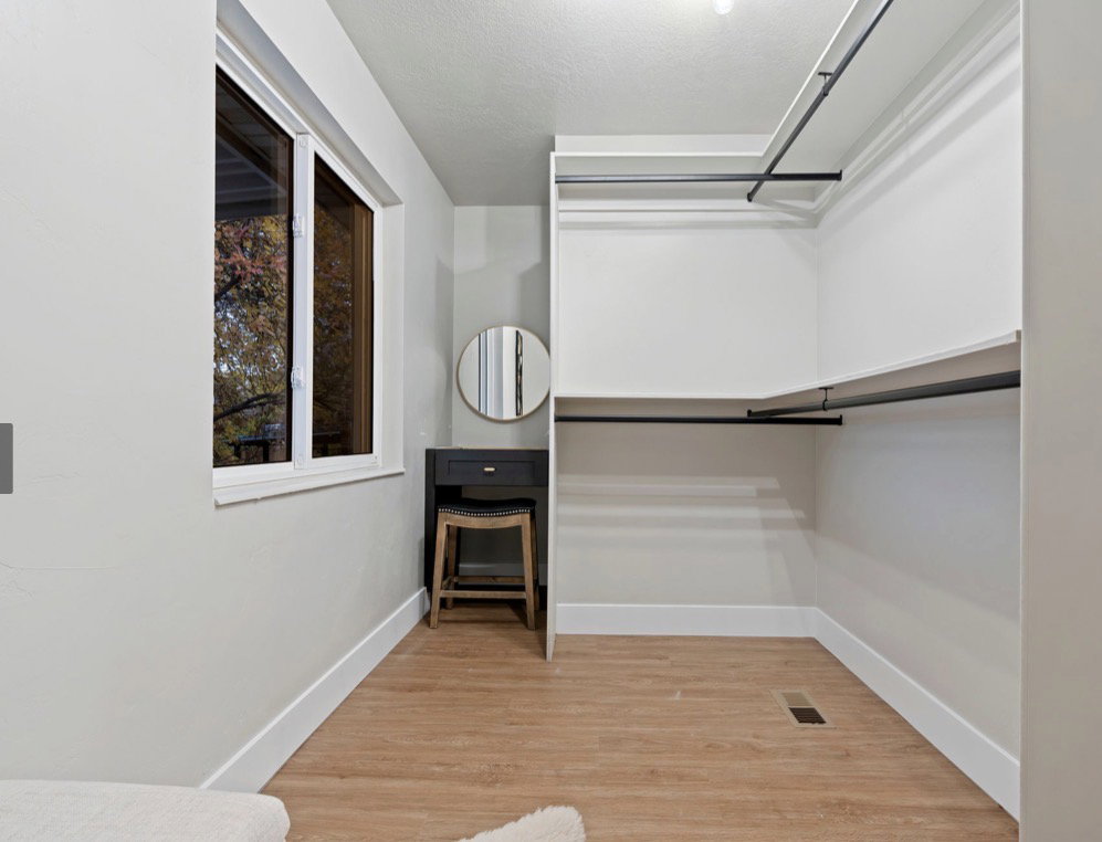 Walk-in closet with integrated shelving and hanging rods, wood-finish flooring, a double-paned window, and a built-in vanity area