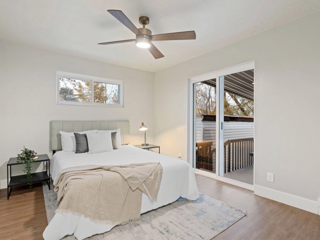Bedroom featuring wood-finish flooring, a contemporary ceiling fan with integrated lighting, a horizontal window, and a sliding glass door leading to an outdoor deck area
