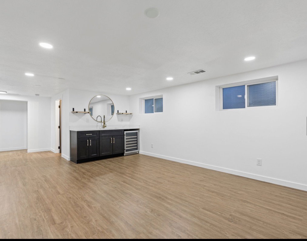 Wood-finish flooring throughout the open space, featuring a built-in wet bar with dark cabinetry, a light-toned countertop, and a beverage cooler