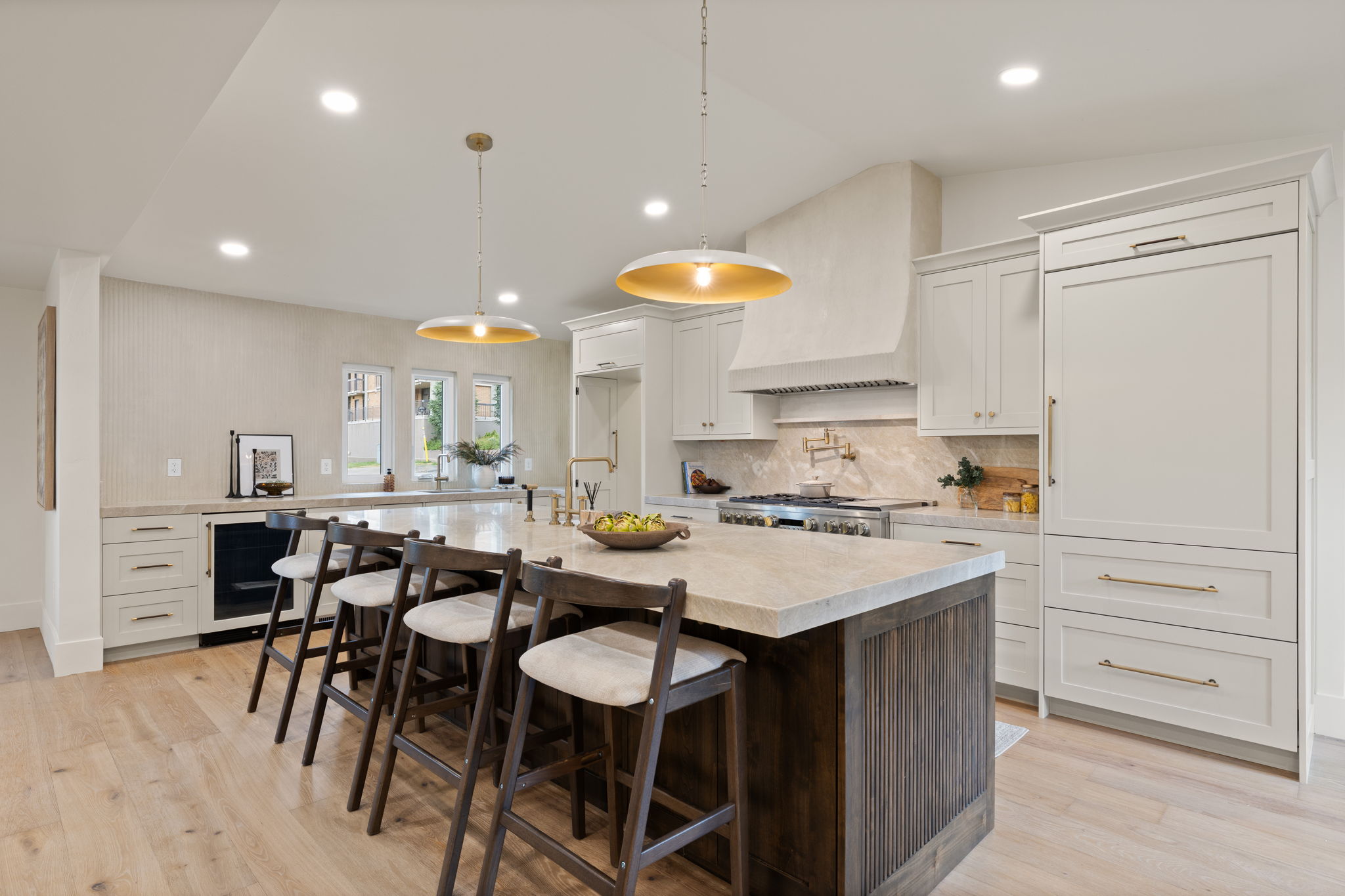 Kitchen featuring a large central island with seating, integrated paneled refrigerator, built-in beverage cooler, custom range hood, and light wood-finish flooring