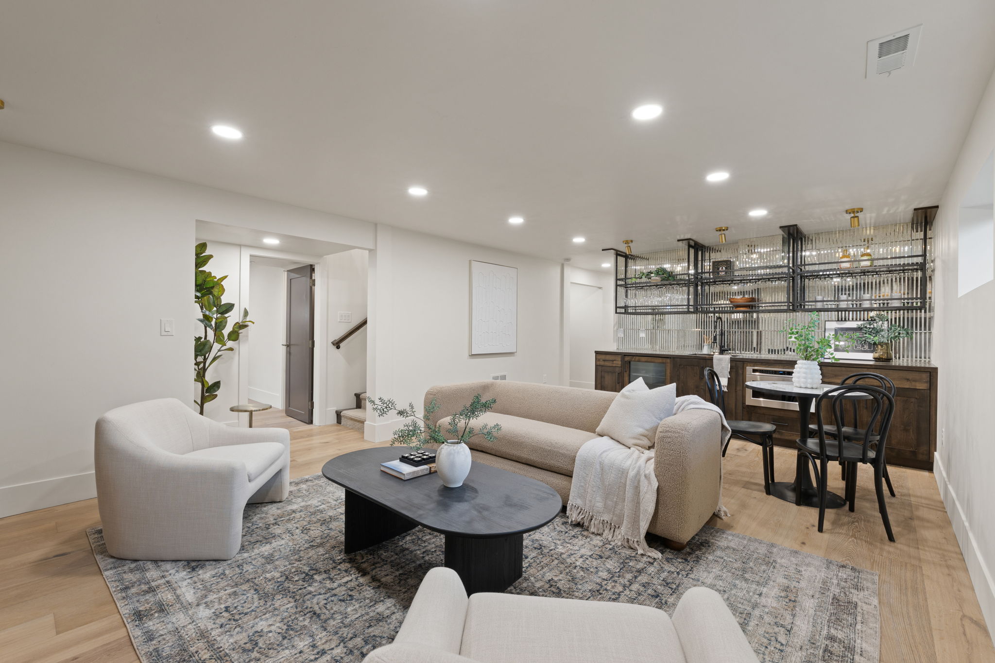 Open-concept living area featuring light wood-finish flooring, recessed lighting, and a built-in wet bar with dark wood cabinetry