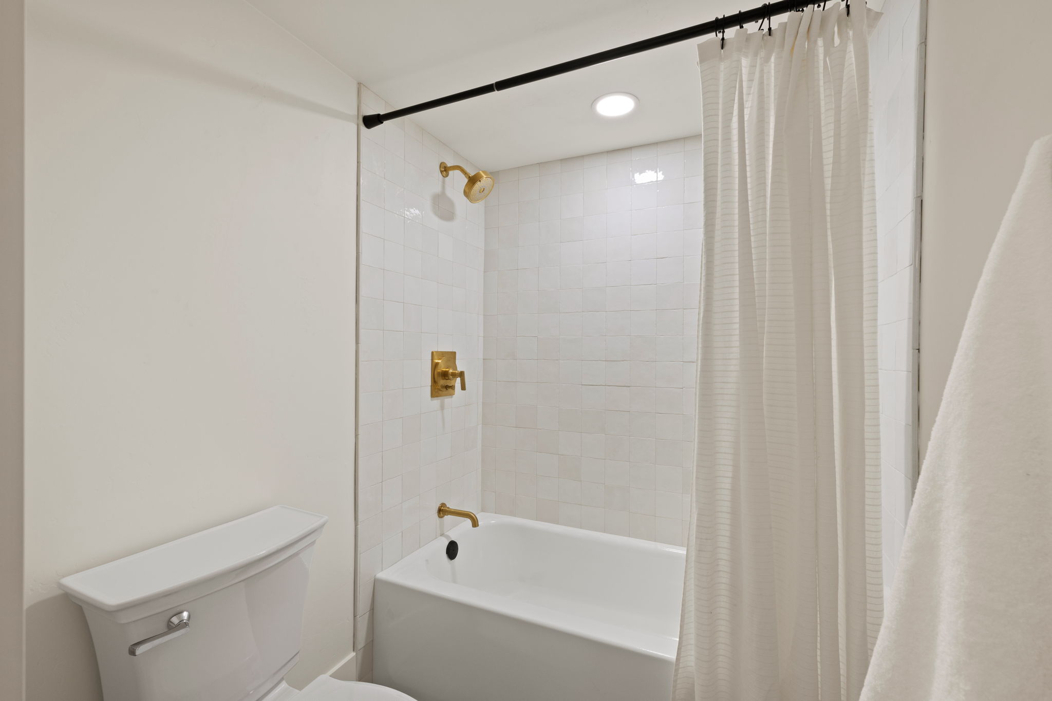 Bathtub and shower combination featuring white subway tile surround, gold-finish fixtures, and recessed lighting