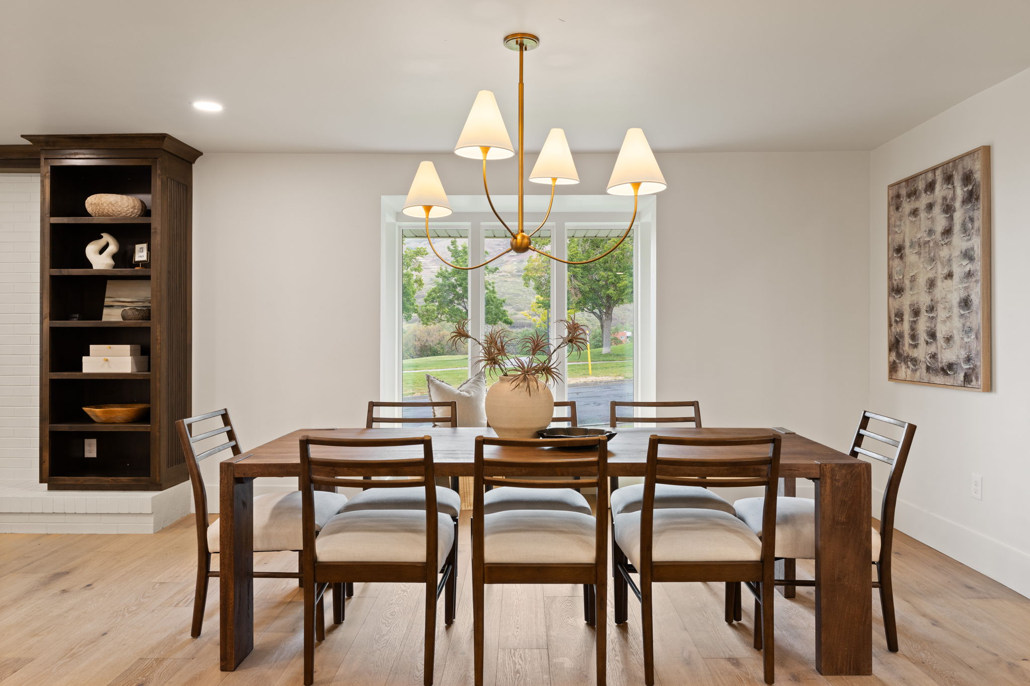 Dining area featuring a contemporary chandelier with conical shades, light wood-finish flooring, and a built-in dark wood cabinetry unit