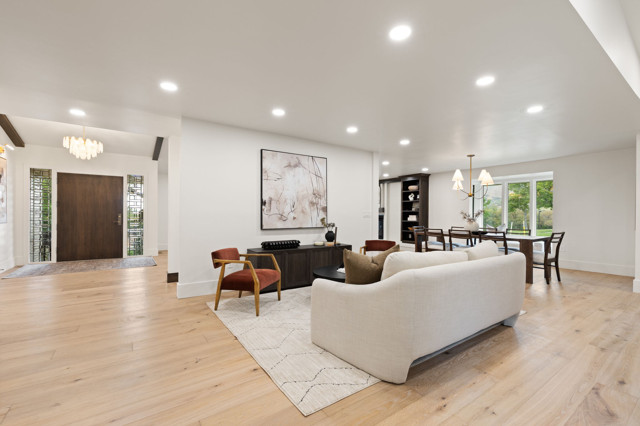 Expansive living area showcasing light wood-finish flooring, recessed lighting, and a white color palette