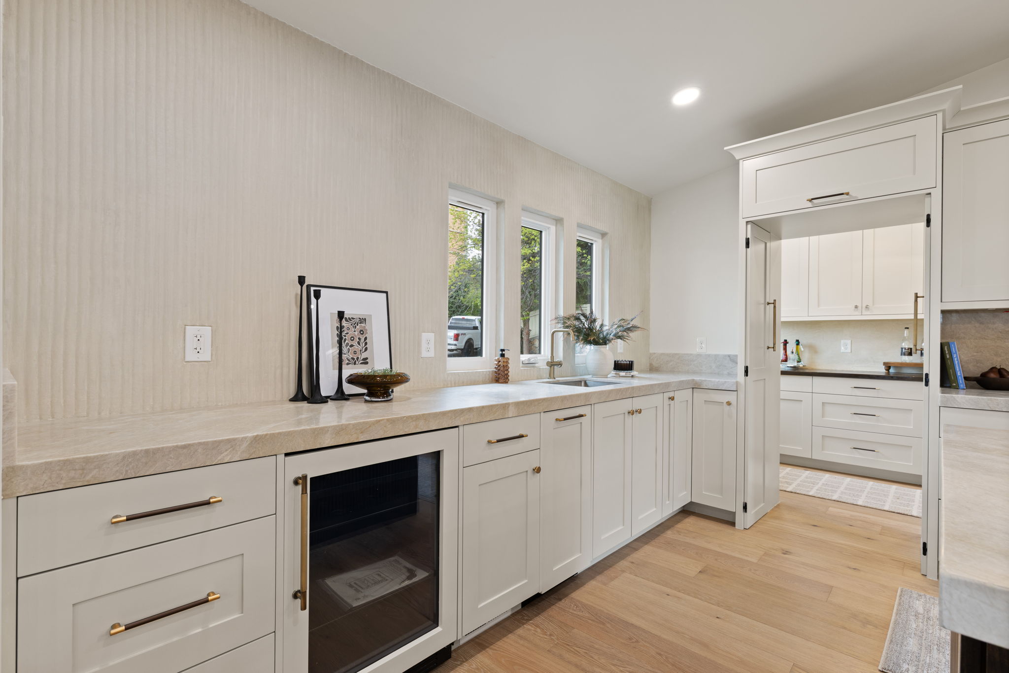 Kitchen area featuring light wood-finish flooring, white cabinetry with dark pulls, a built-in beverage refrigerator, and light-toned countertops