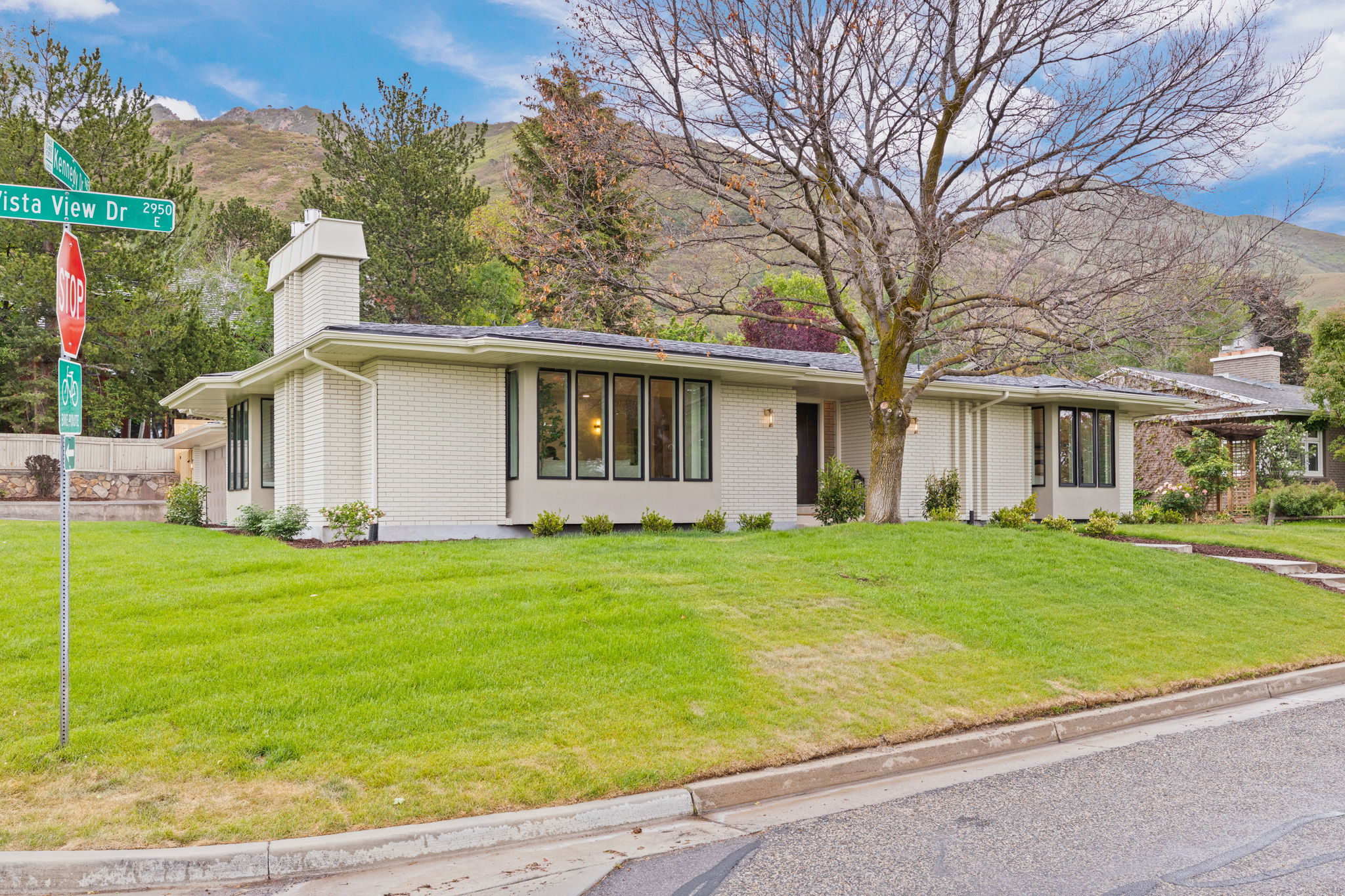 Mid-century modern exterior featuring light brick siding, a prominent chimney, and a dark asphalt shingle roof