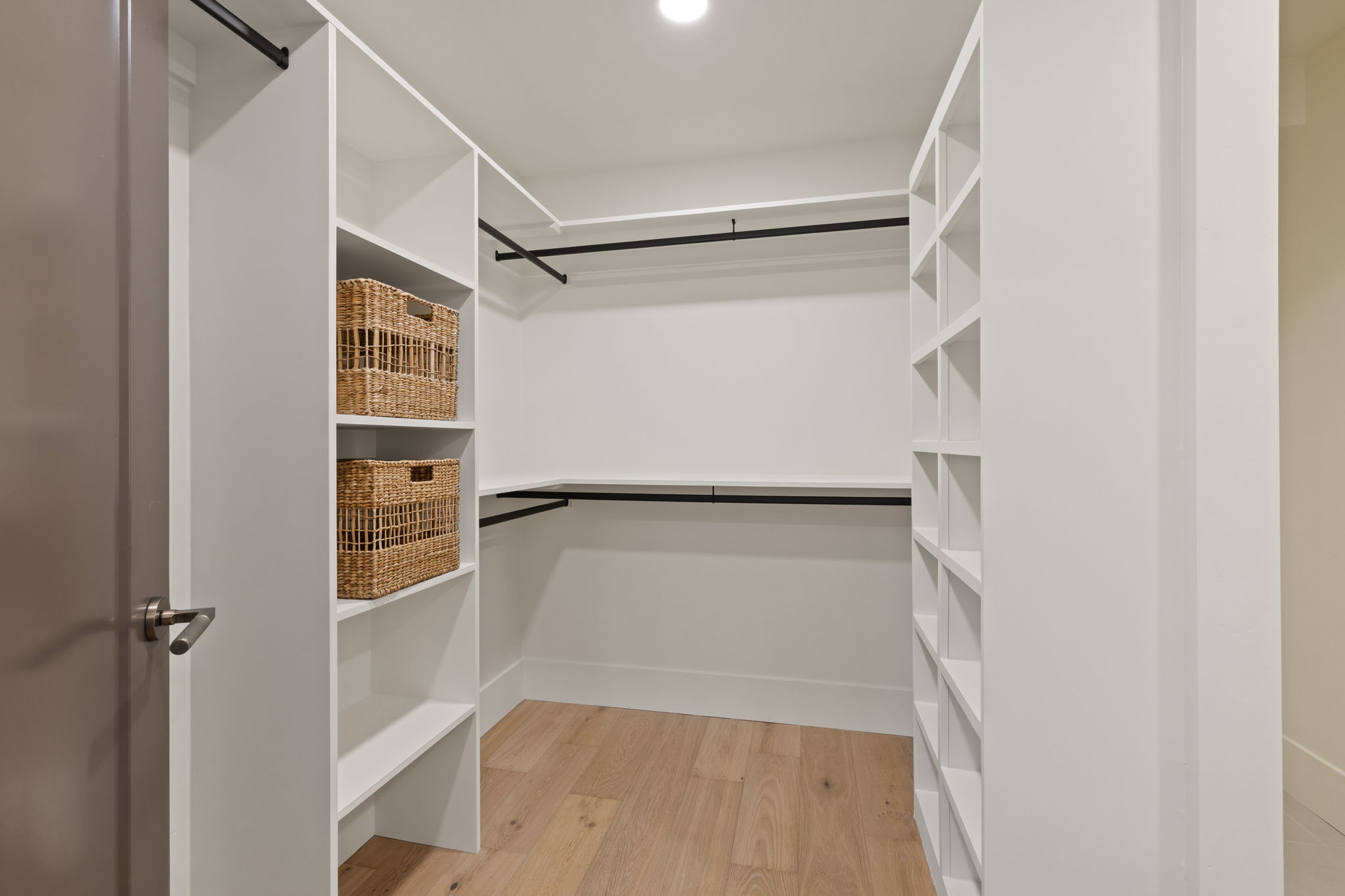 Custom walk-in closet featuring white shelving, multiple hanging rods, dedicated shoe cubbies, and wood-finish flooring