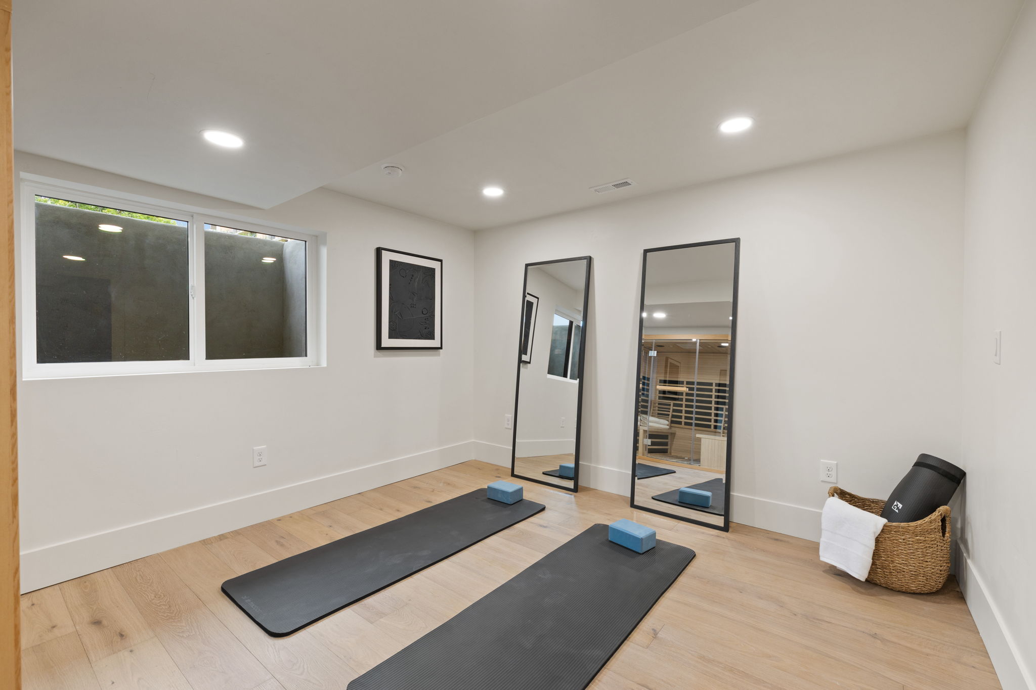 Recessed lighting illuminates this bright room featuring wood-finish flooring, white baseboards, and a window with a deep window well