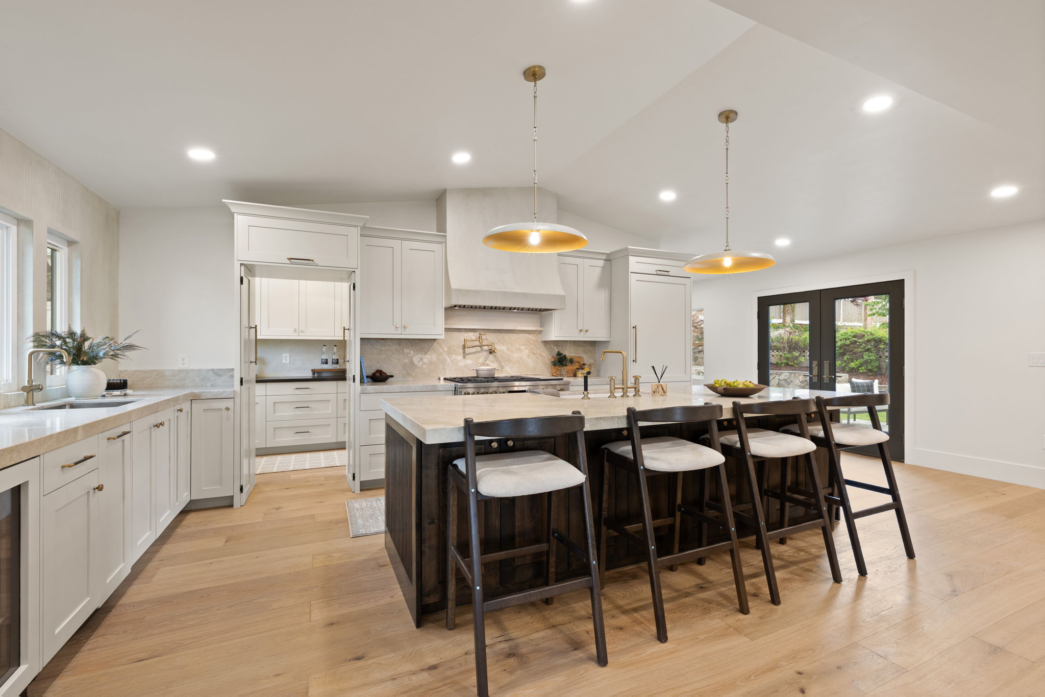 Gourmet kitchen featuring a large central island with seating, light wood-finish flooring, white cabinetry, integrated appliances, and a vaulted ceiling with recessed lighting