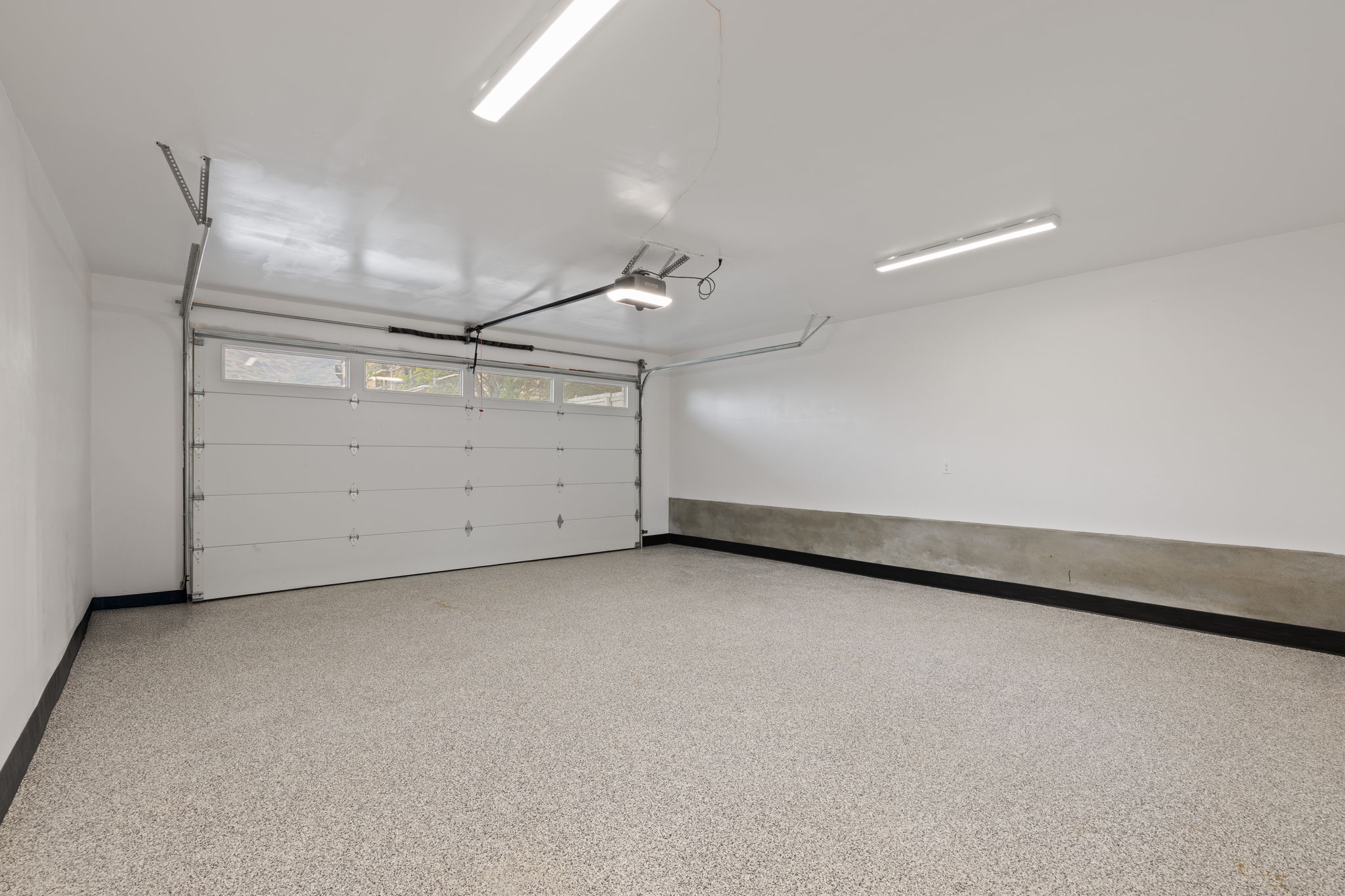Spacious garage featuring a sectional overhead door with upper window panels, automated opener, and speckled epoxy flooring