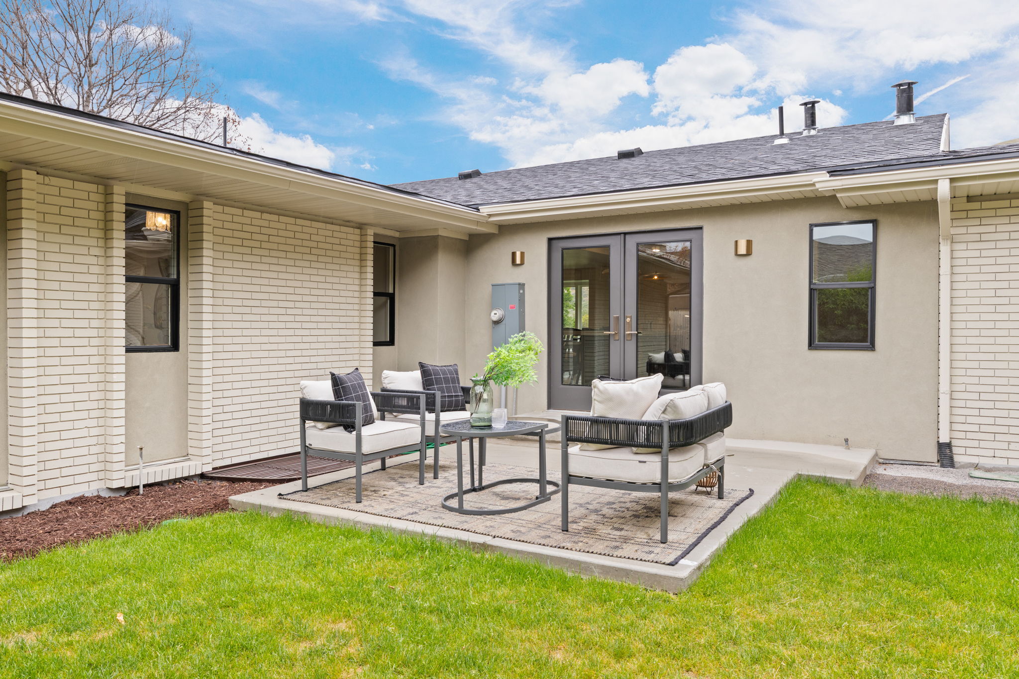 Outdoor patio featuring a concrete slab, double French doors, black window frames, stucco siding, and light brick exterior