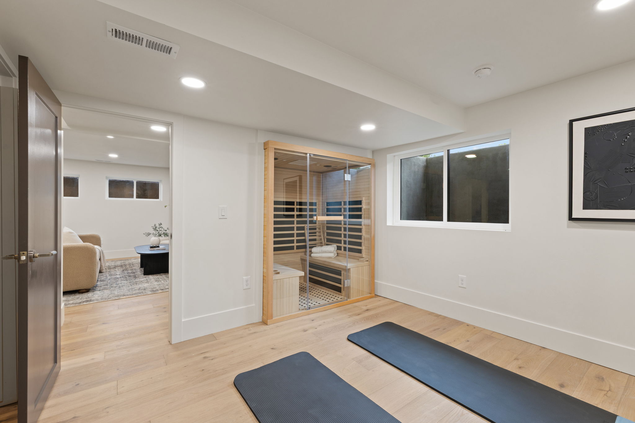 Dedicated wellness space featuring a built-in sauna, light wood-finish flooring, recessed lighting, white baseboards, and a white-framed window
