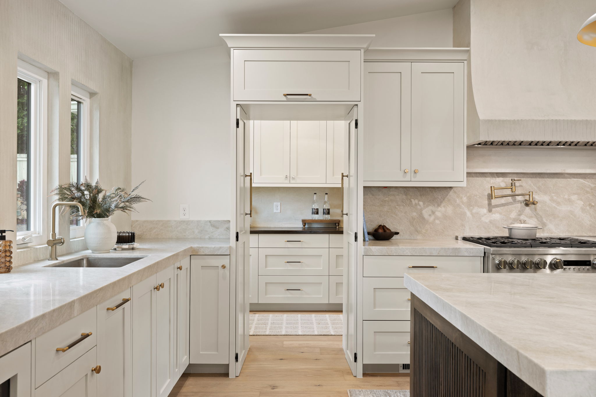 Gourmet kitchen featuring a stainless steel range with a pot filler, light-toned countertops, white cabinetry with brass hardware, and wood-finish flooring