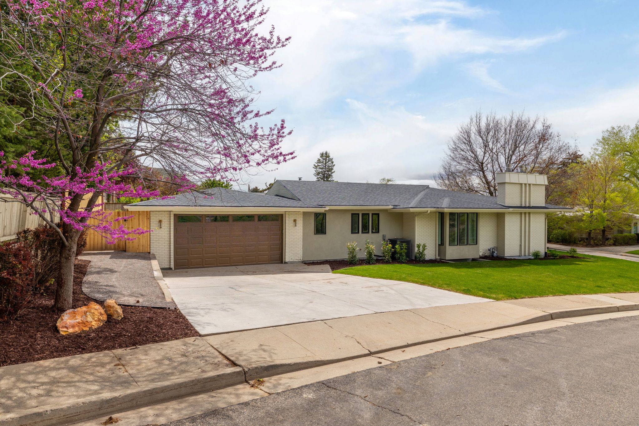 Contemporary single-story residence featuring a two-car garage with a brown panel door, a paved driveway, and a front yard with manicured lawn