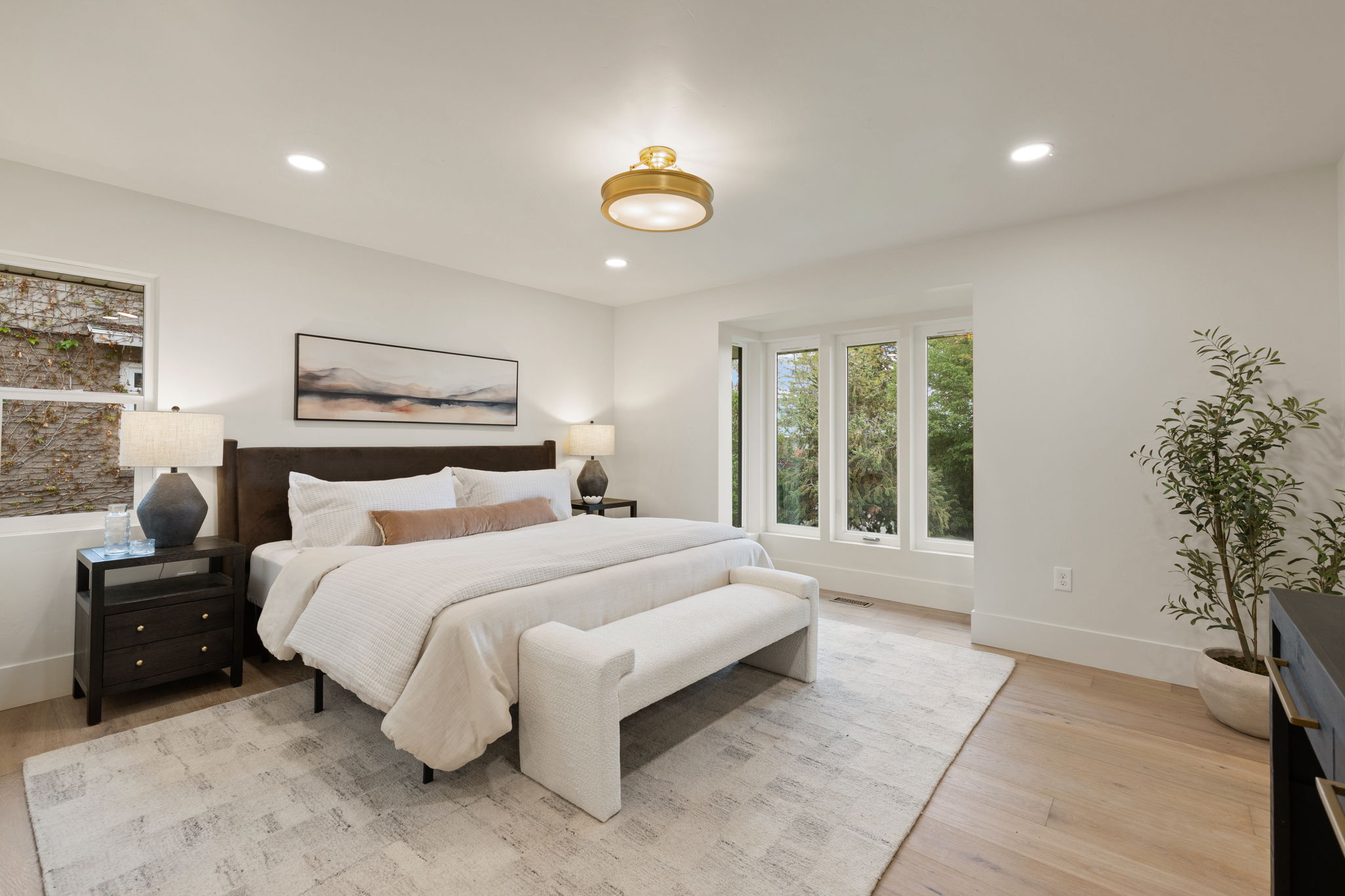 Recessed lighting and a central gold-finish ceiling fixture illuminate this bedroom featuring light wood-finish flooring