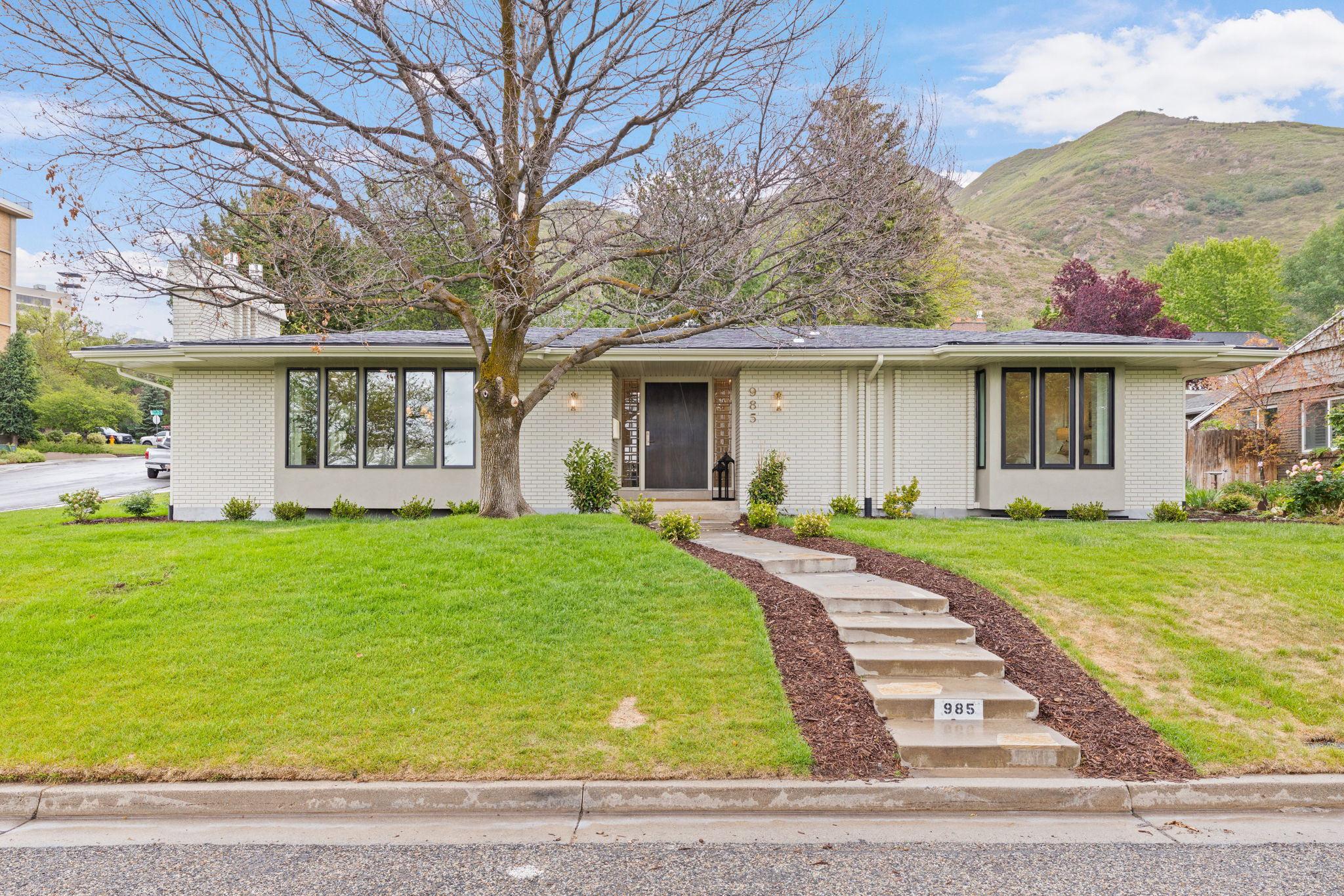 Mid-century modern residence featuring light-colored brick facade and a dark asphalt shingle roof