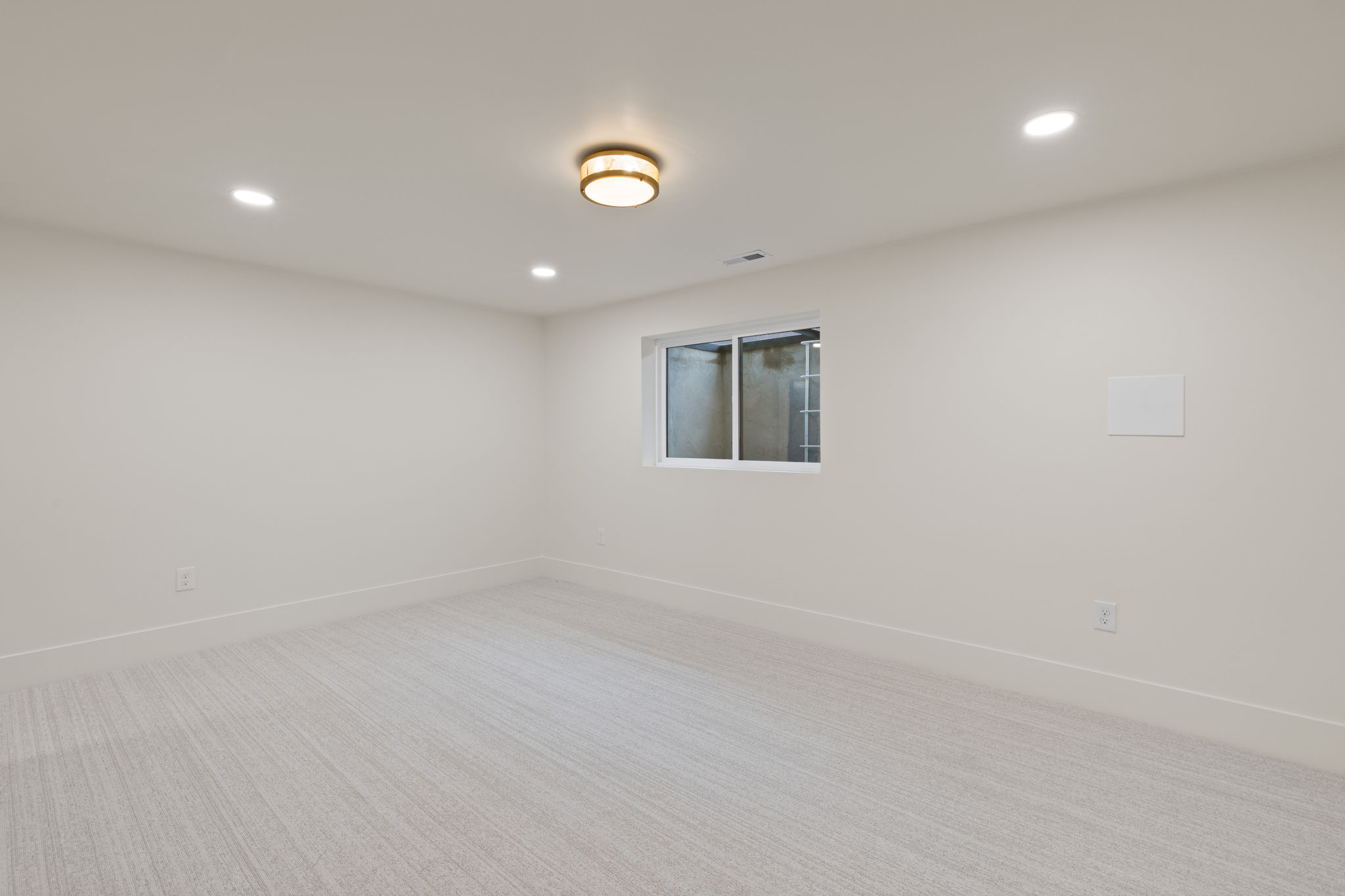 Spacious room featuring light-toned carpet, white walls, and bright overhead lighting