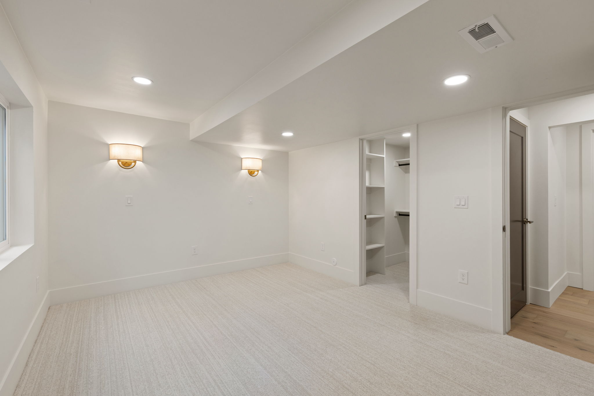 Spacious room featuring light-toned carpeting, recessed lighting, and two wall sconces