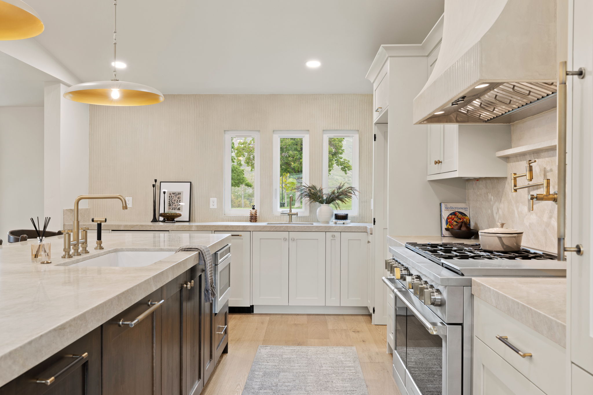 Gourmet kitchen featuring a substantial island with an integrated sink and microwave drawer, light wood-finish flooring, white perimeter cabinetry, stone countertops, and a professional-grade range with a custom hood
