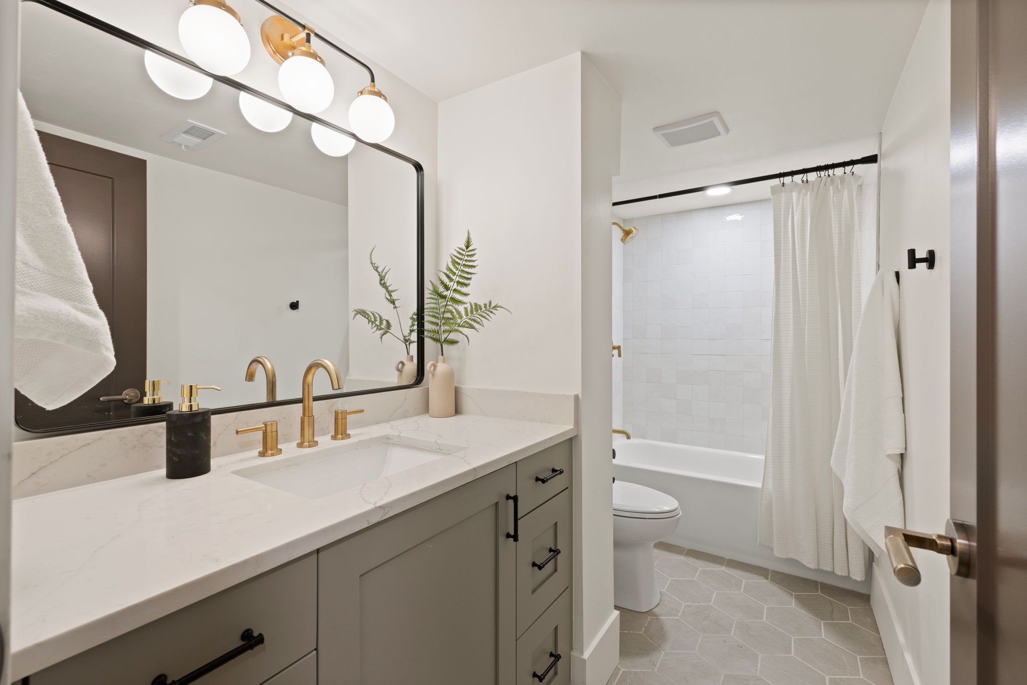 Bathroom featuring a light-toned vanity with a built-in sink, gold-finish faucet, and a large rectangular mirror