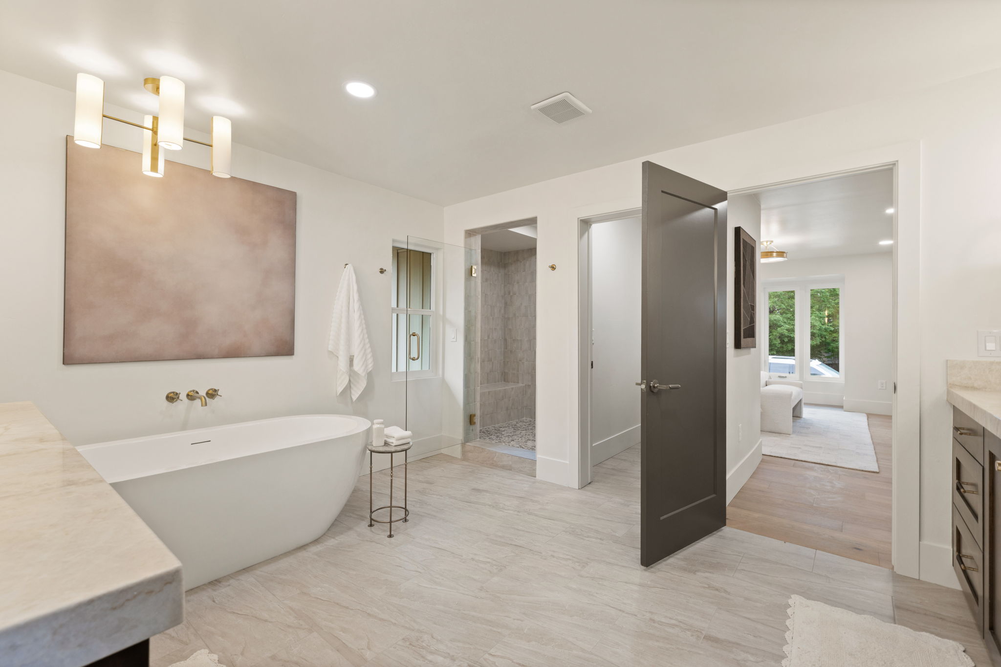 Spacious bathroom featuring a freestanding soaking tub with wall-mounted brass fixtures, a glass-enclosed shower, wood-finish flooring, and light-toned tile flooring