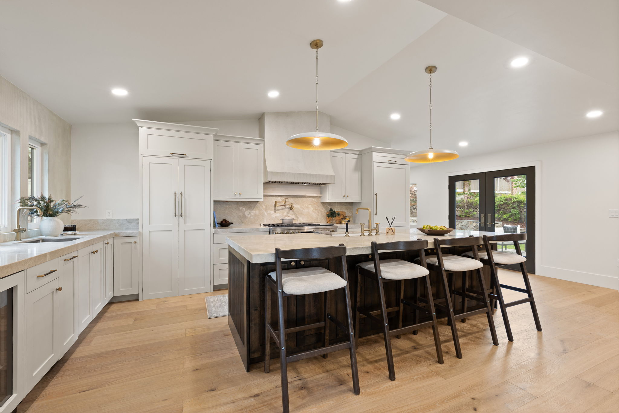 Spacious kitchen featuring light wood-finish flooring, white cabinetry, integrated appliances, a central island with a light-toned countertop, and recessed lighting