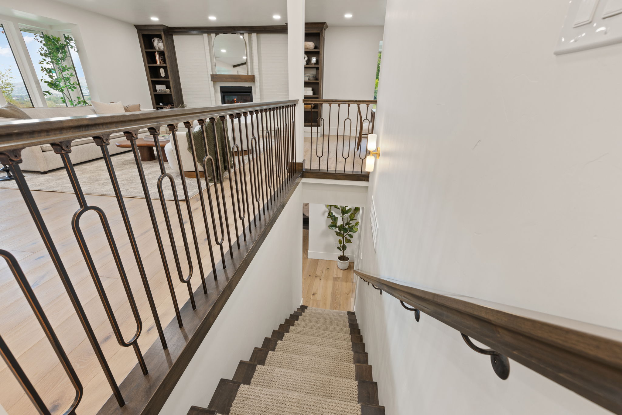 Staircase featuring dark wood handrails, decorative metal balusters, and carpeted treads, with light wood-finish flooring visible on the upper level