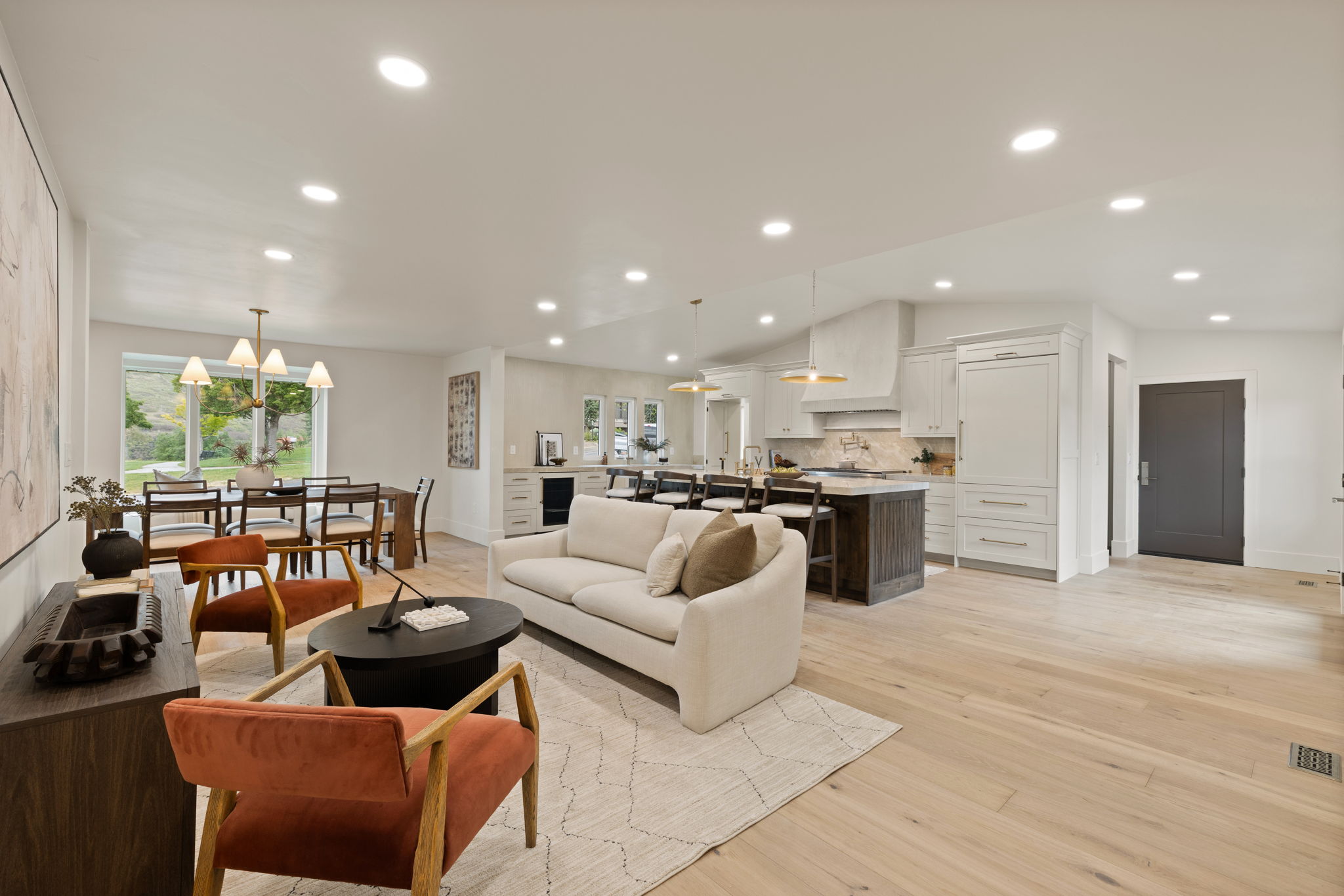 Open-concept living space featuring light wood-finish flooring, recessed lighting, a modern kitchen with a large island and light-toned cabinetry, and a dining area with a contemporary chandelier