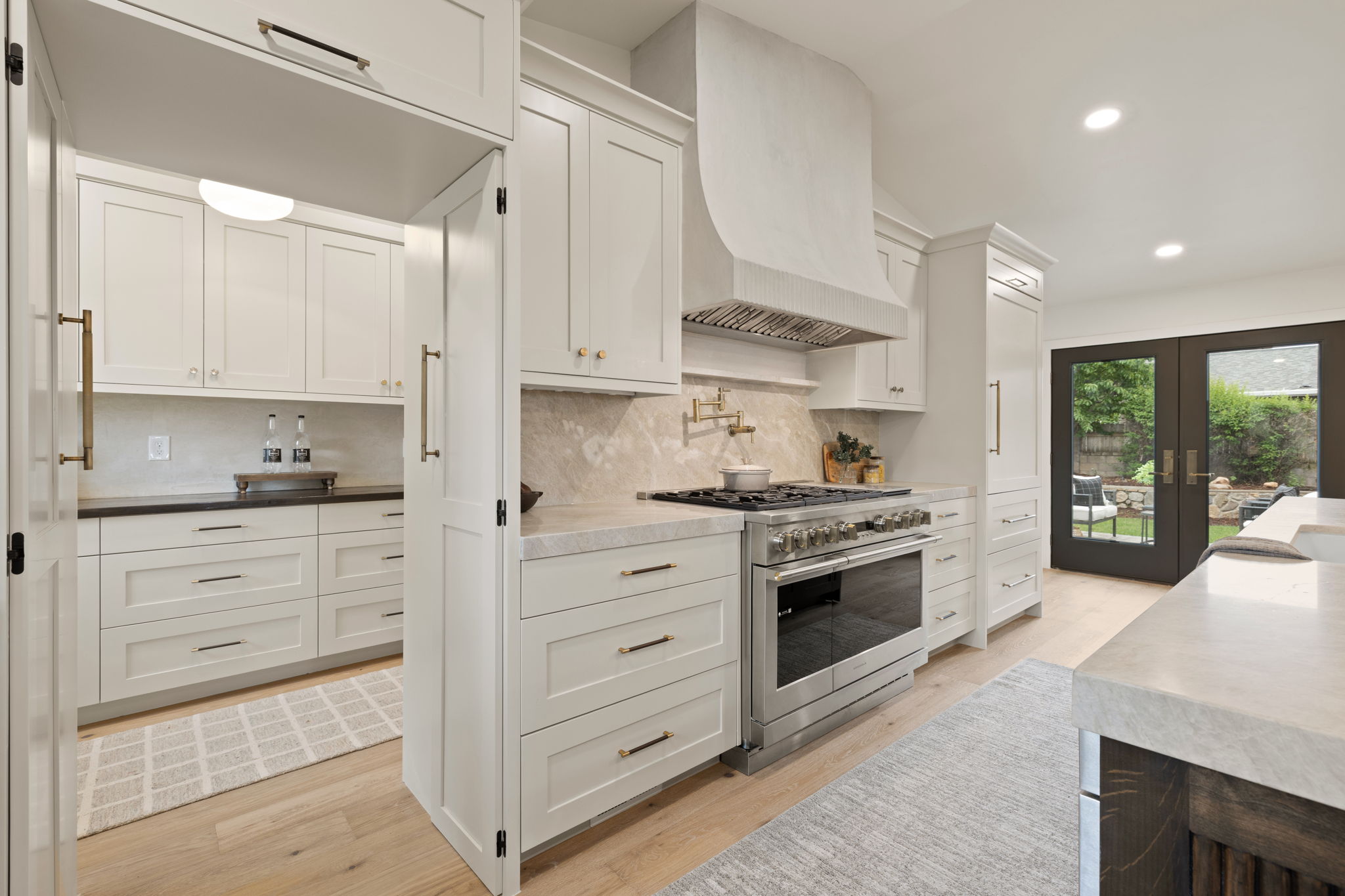 Modern kitchen featuring light-toned cabinetry, a built-in stainless steel range, and a custom range hood