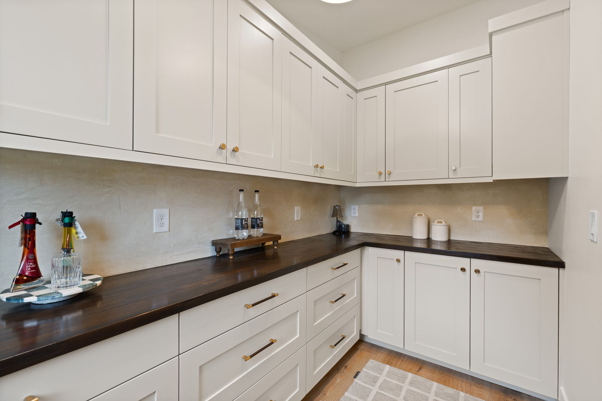Corner pantry or butler's pantry featuring extensive white shaker cabinetry, dark wood-finish countertops, and a textured backsplash