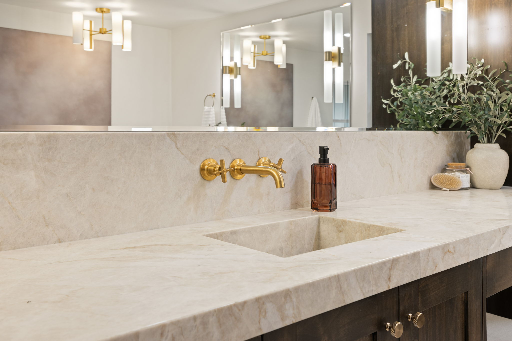 Integrated stone sink with a wall-mounted brass faucet, set within a light-toned countertop