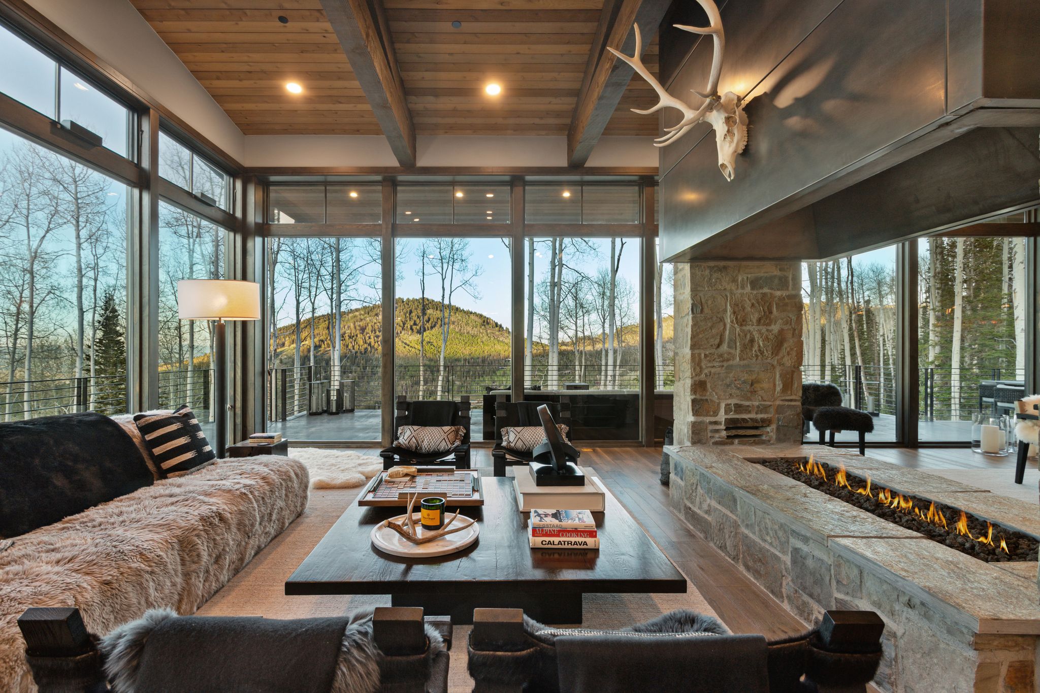 Living area featuring a floor-to-ceiling window wall, wood-finish flooring, a wood plank and beam ceiling, a stone fireplace, and a linear gas fire pit