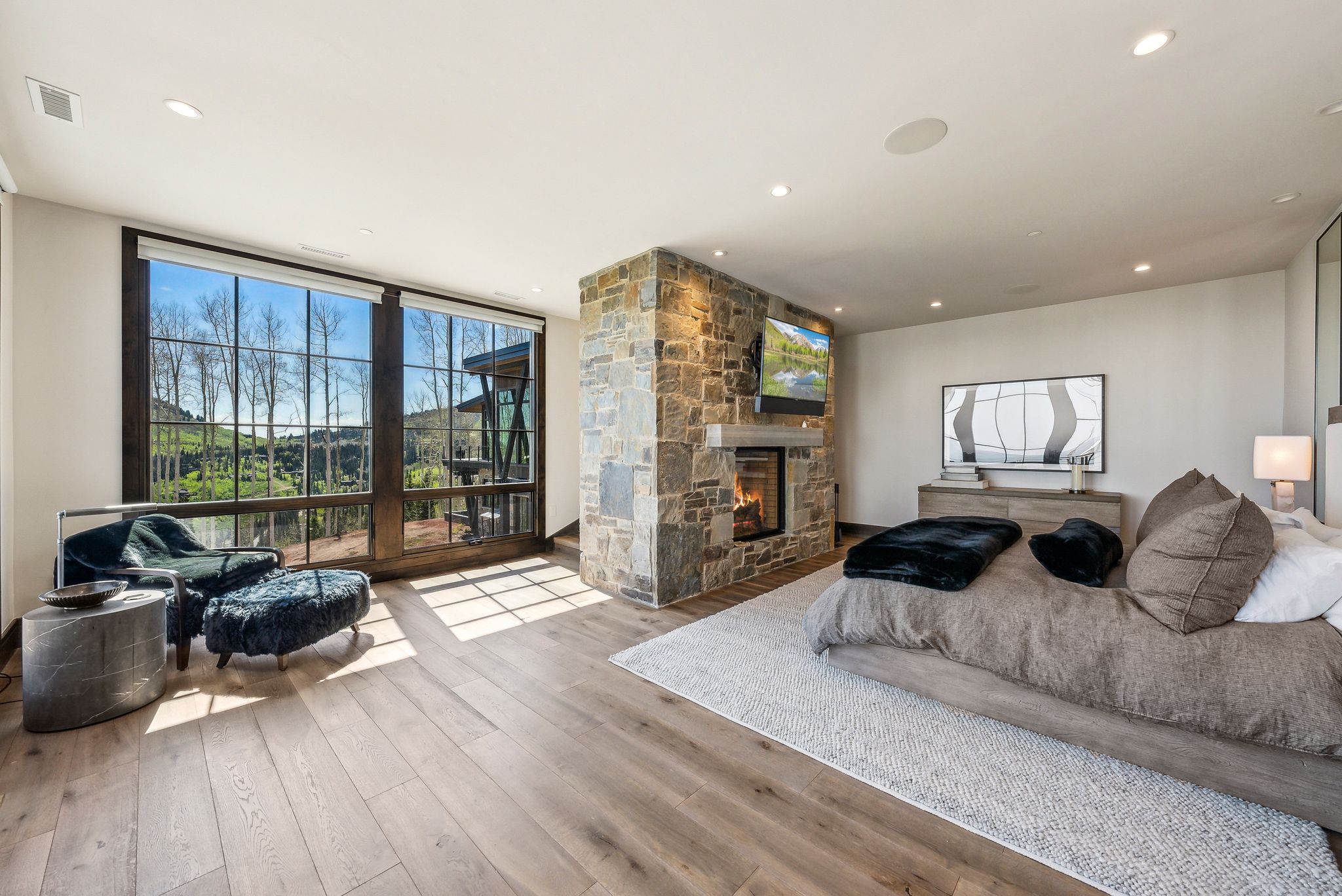 Spacious room featuring extensive window framing, stone-clad fireplace with mantel, recessed lighting, and wood-finish flooring