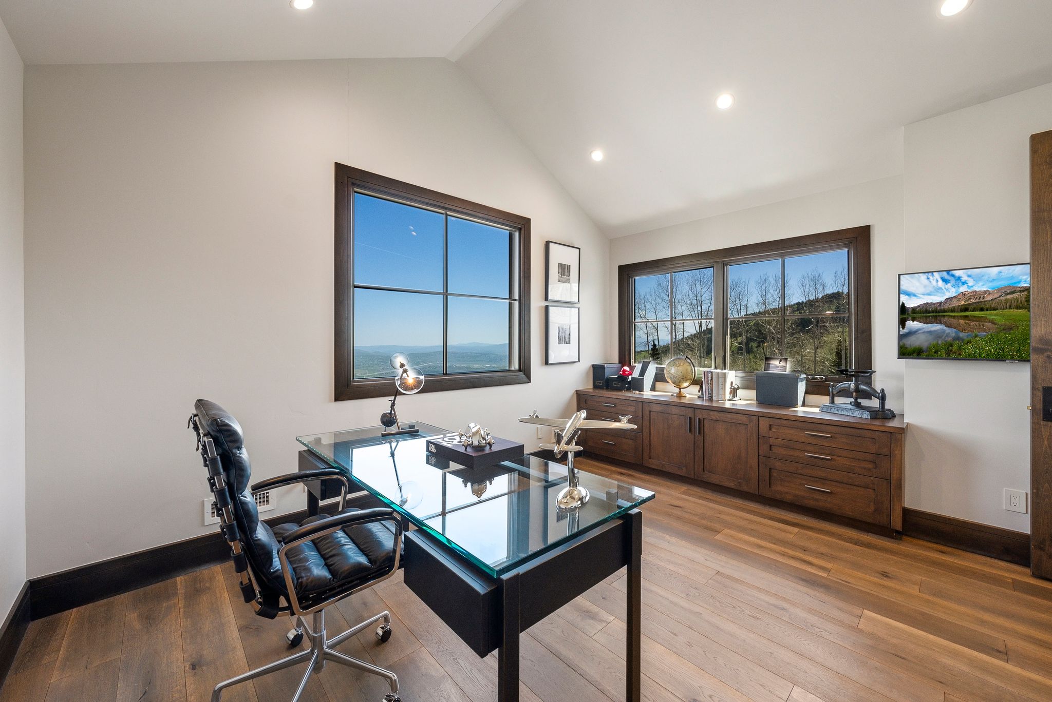 Spacious room featuring vaulted ceilings, recessed lighting, wood-finish flooring, and expansive windows with dark wood frames