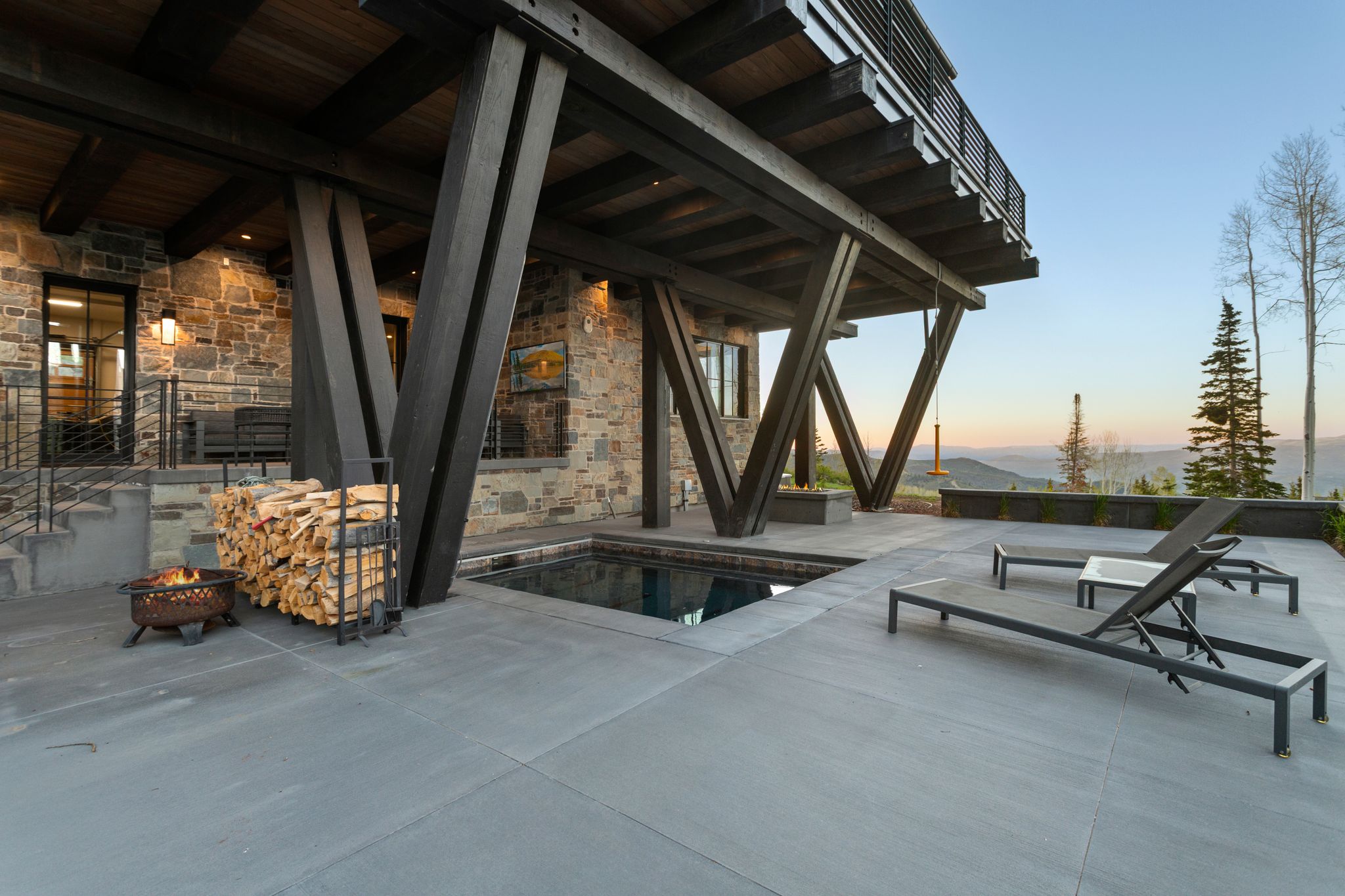 Exterior patio featuring a built-in spa, expansive concrete hardscaping, and a stone-clad facade with dark window frames