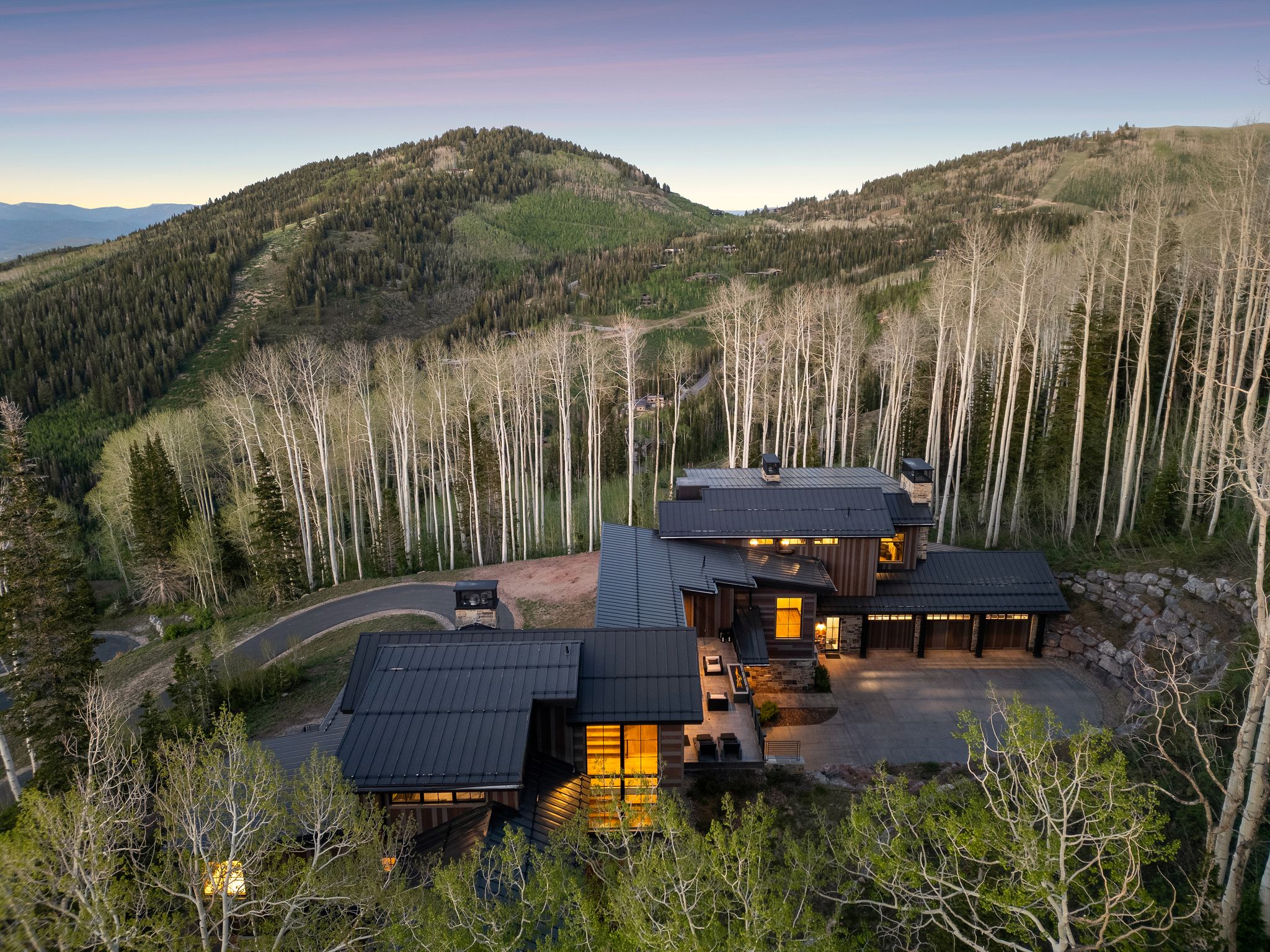 Contemporary mountain residence featuring multiple levels, extensive dark-toned metal roofing, and multiple garages with wood-paneled doors