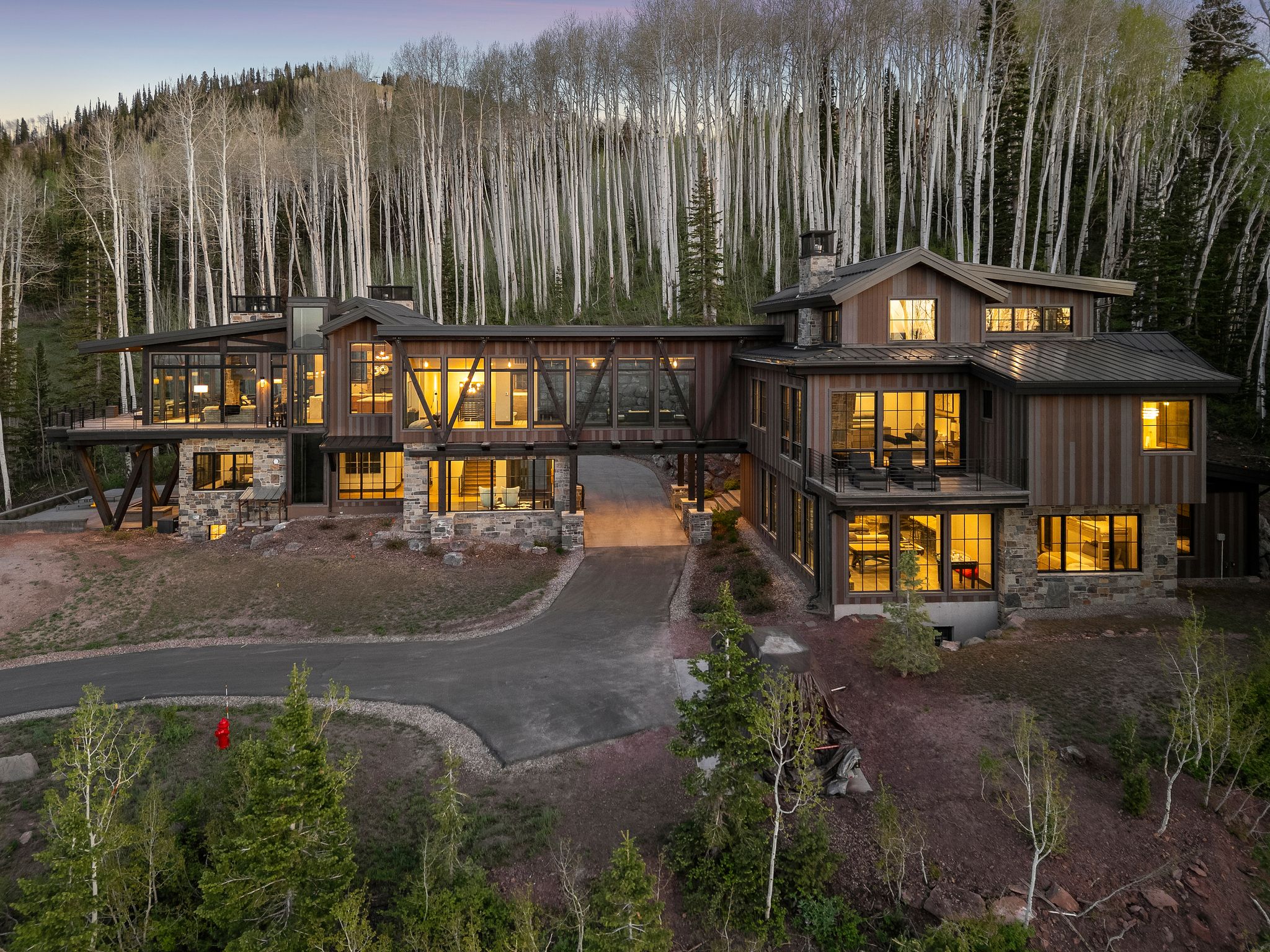 Expansive contemporary residence featuring multiple levels, extensive glazing, a stone and wood siding exterior, a covered entryway, and mature trees surrounding the property