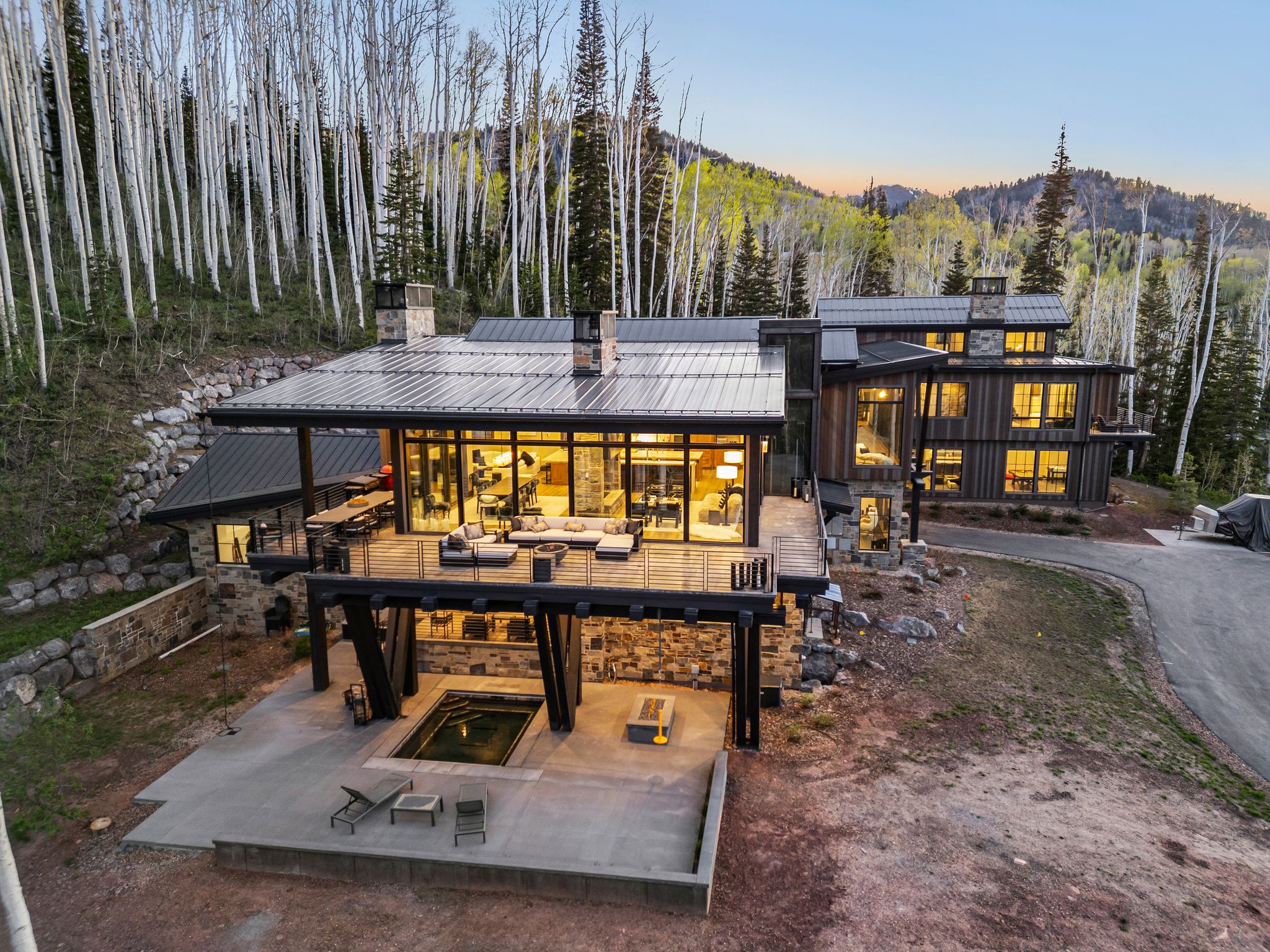 Multi-level contemporary residence featuring extensive glass window walls, a spacious outdoor deck, a lower patio with an in-ground spa, and stone and wood siding