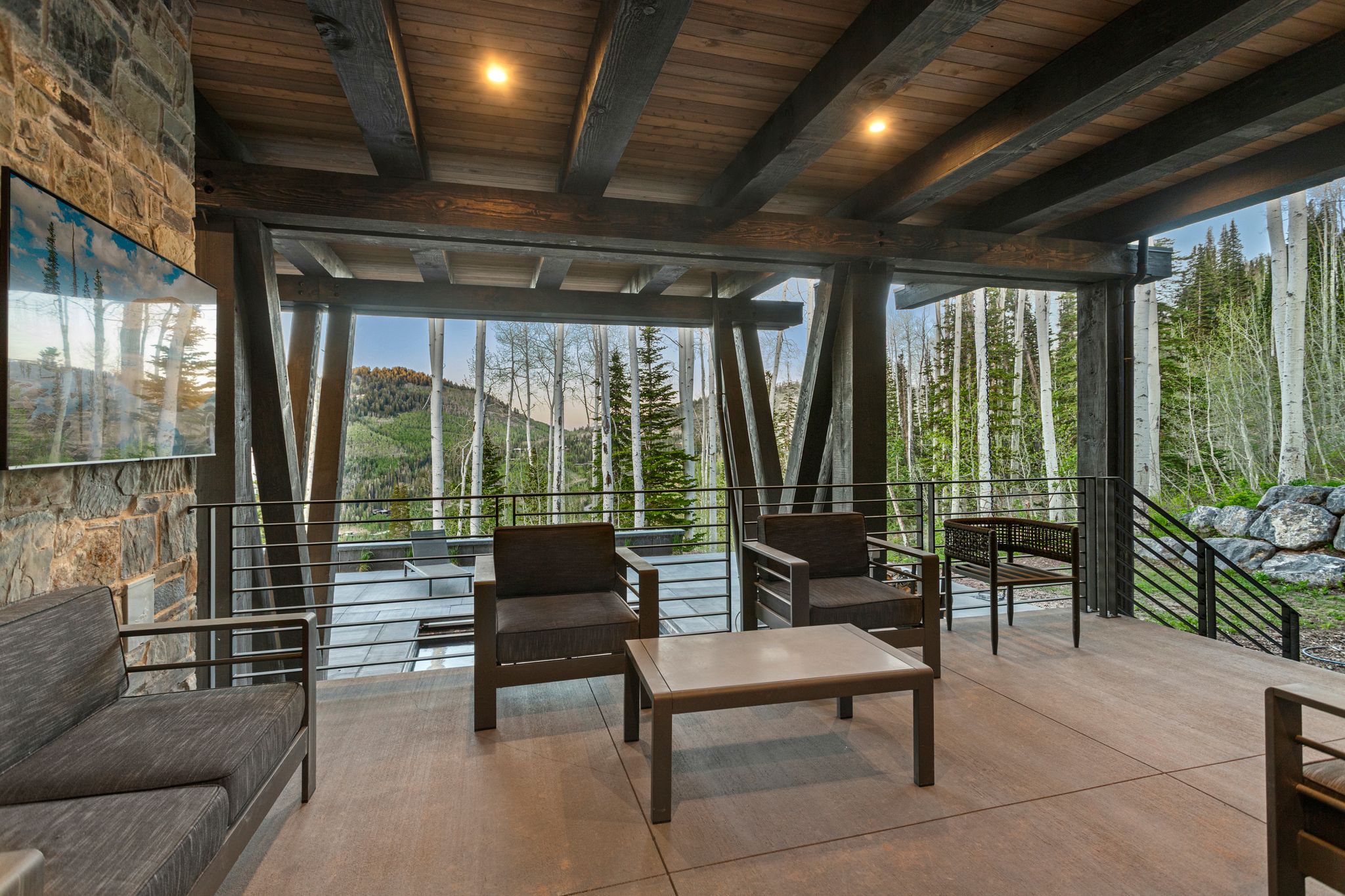 Spacious outdoor patio featuring stone accent wall, wood-paneled ceiling with exposed beams, recessed lighting, and a metal railing system